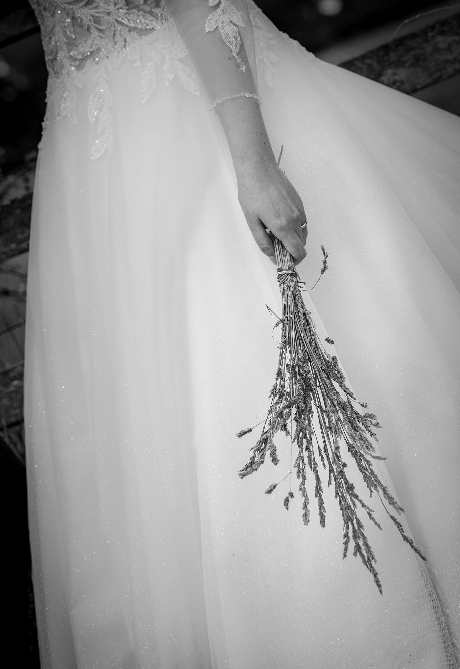 Bride in white lace wedding gown holding a bundle of dried lavender flowers, black and white photo.