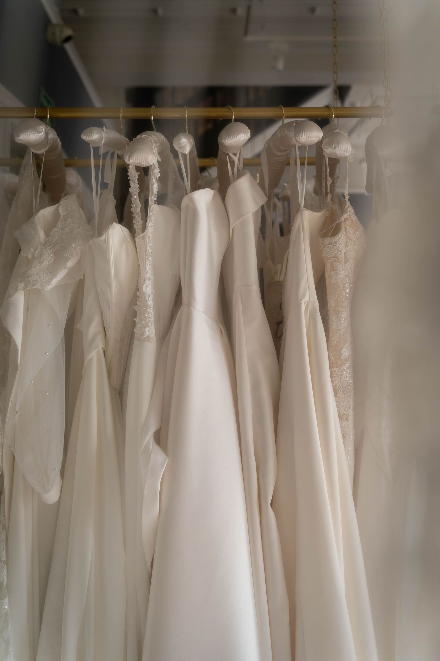 A row of elegant white and ivory wedding dresses hanging on gold hangers in a bridal boutique.