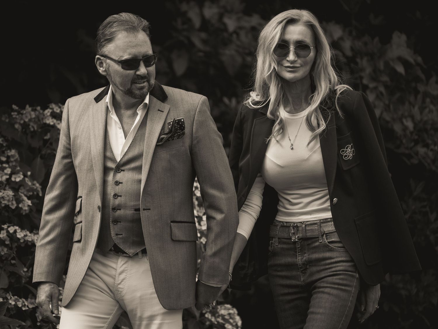 A stylish couple walks together outdoors in coordinated formal attire.