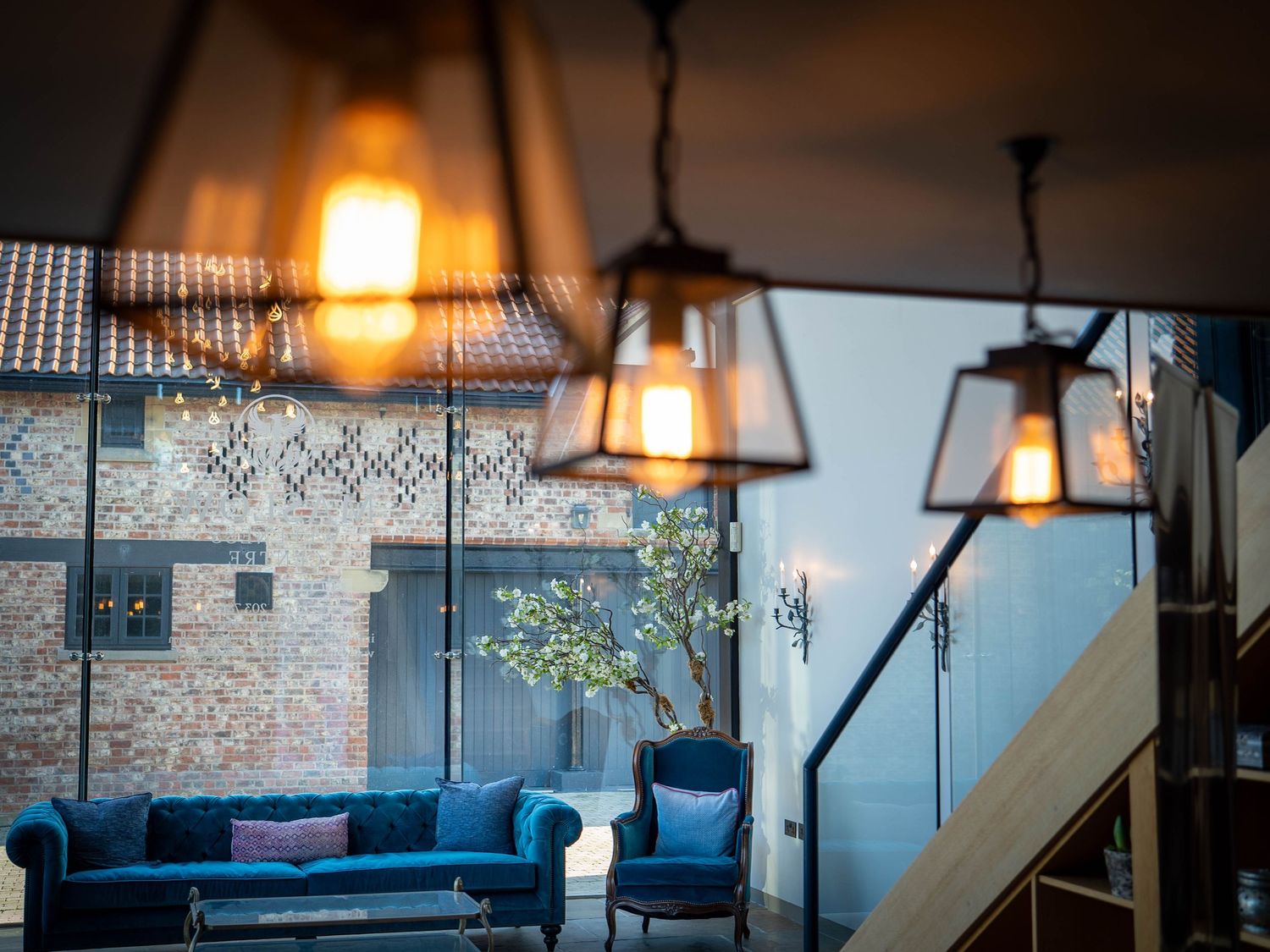 Modern living room interior with blue velvet sofa, industrial pendant lights, and decorative wallpaper accent wall.