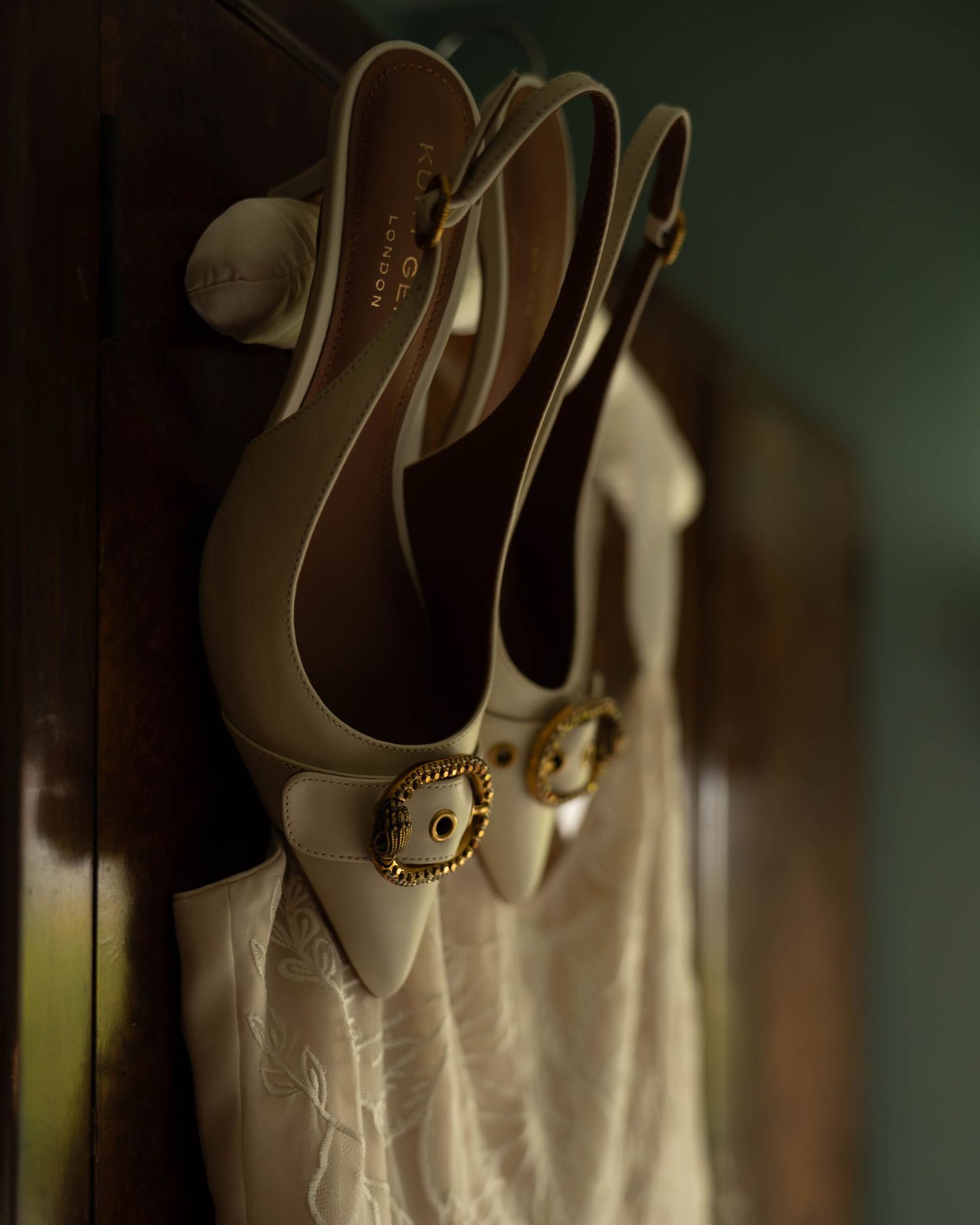 Cream slingback heels with gold buckles hanging on a wooden wardrobe door.