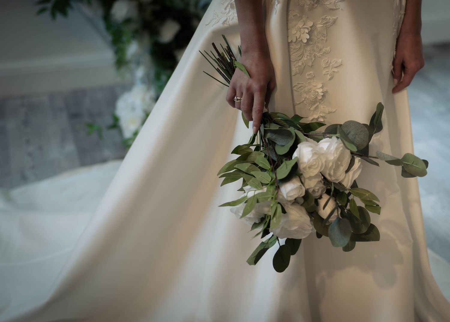 Bride in white wedding gown holding elegant bouquet of white peonies and greenery.