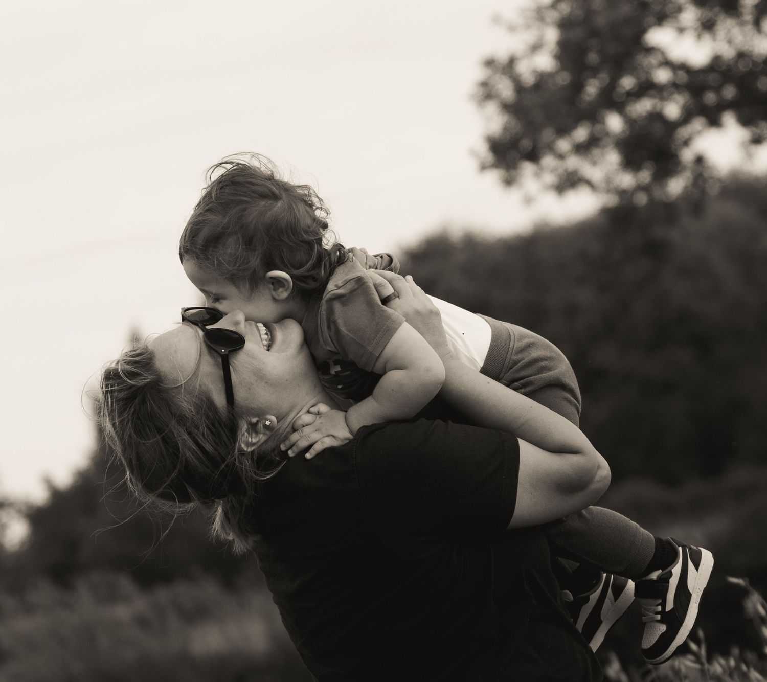 A black and white portrait capturing a joyful embrace between parent and child outdoors.