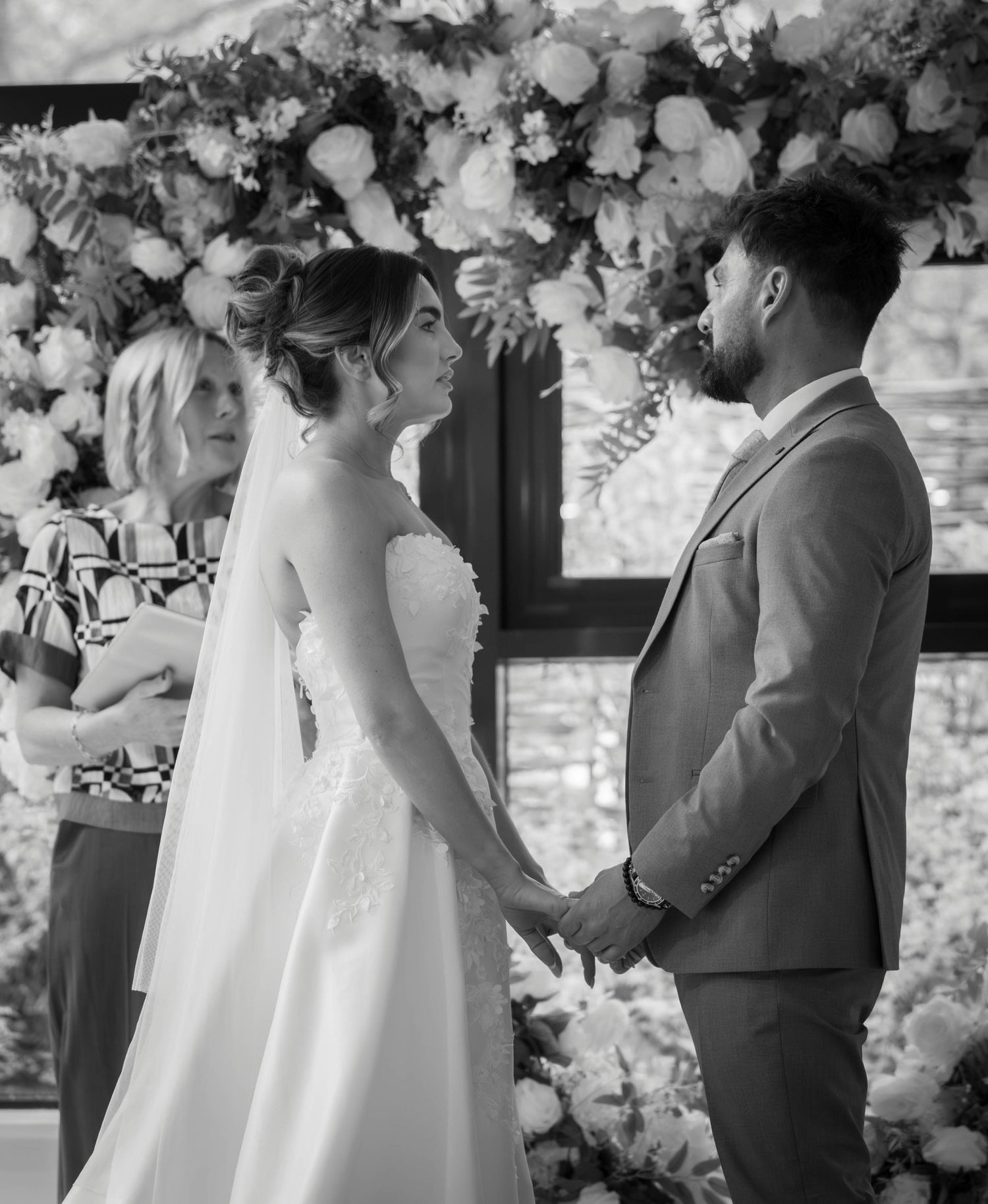 Black and white photo of a bride and groom holding hands at the altar during their wedding ceremony.