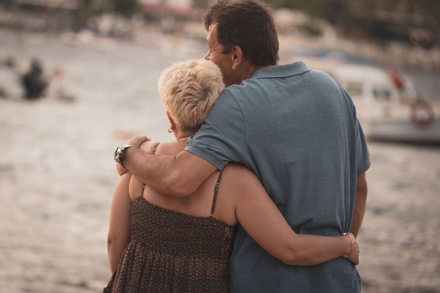 A couple shares an intimate moment against a blurred waterfront background at sunset.