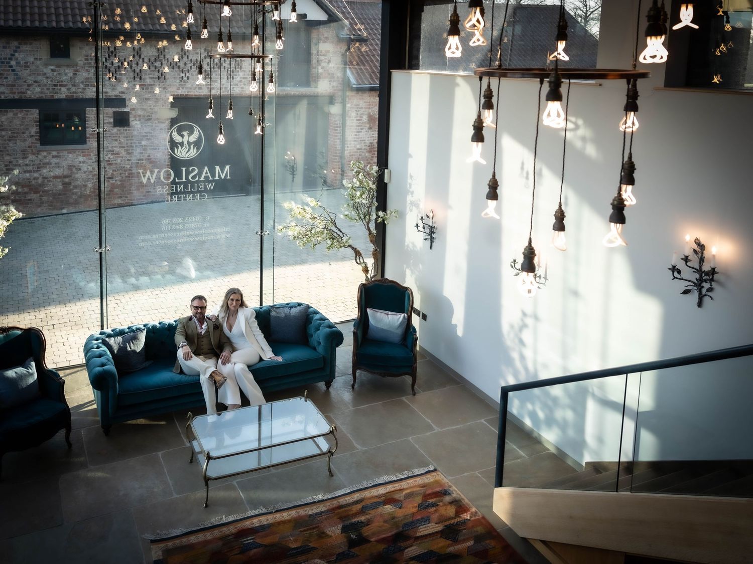 Modern spa interior with teal velvet couch, pendant lights, and white walls creating a serene wellness atmosphere.