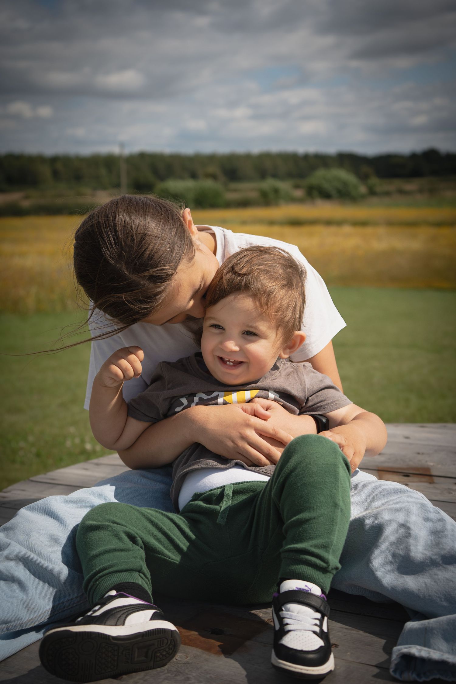 Candid playful moments shared on a blanket in a grassy field under cloudy skies.