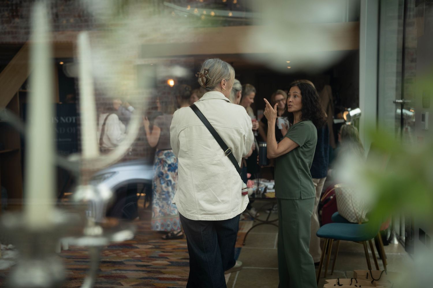 Two people conversing indoors at an event, with soft bokeh lighting and elegant decor in the background.