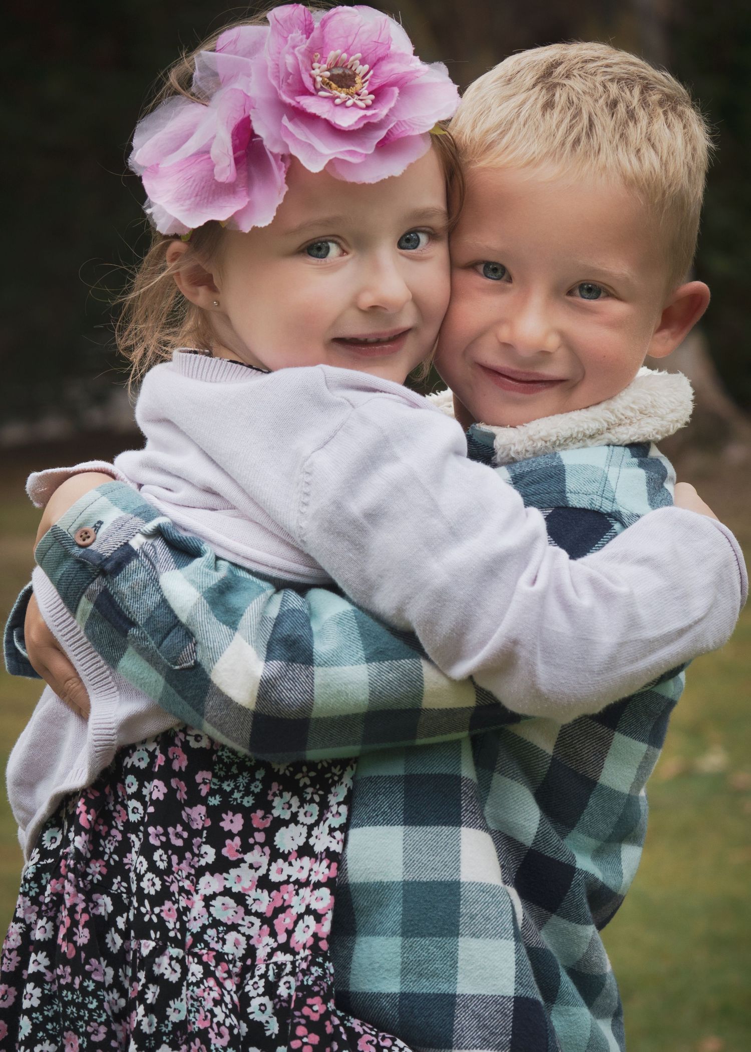 Children wearing plaid and floral patterns share affectionate moments outdoors.