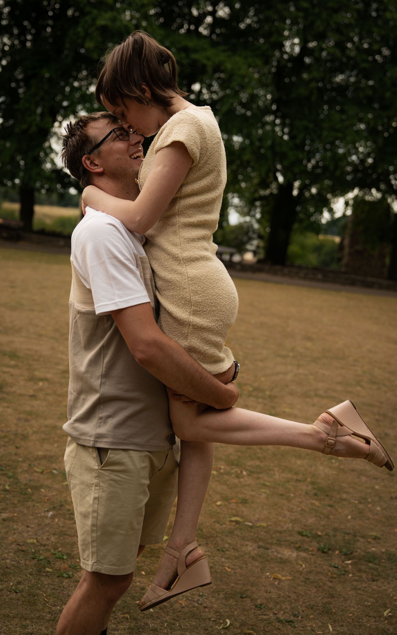 A couple embraces playfully in a park setting during a romantic photoshoot.