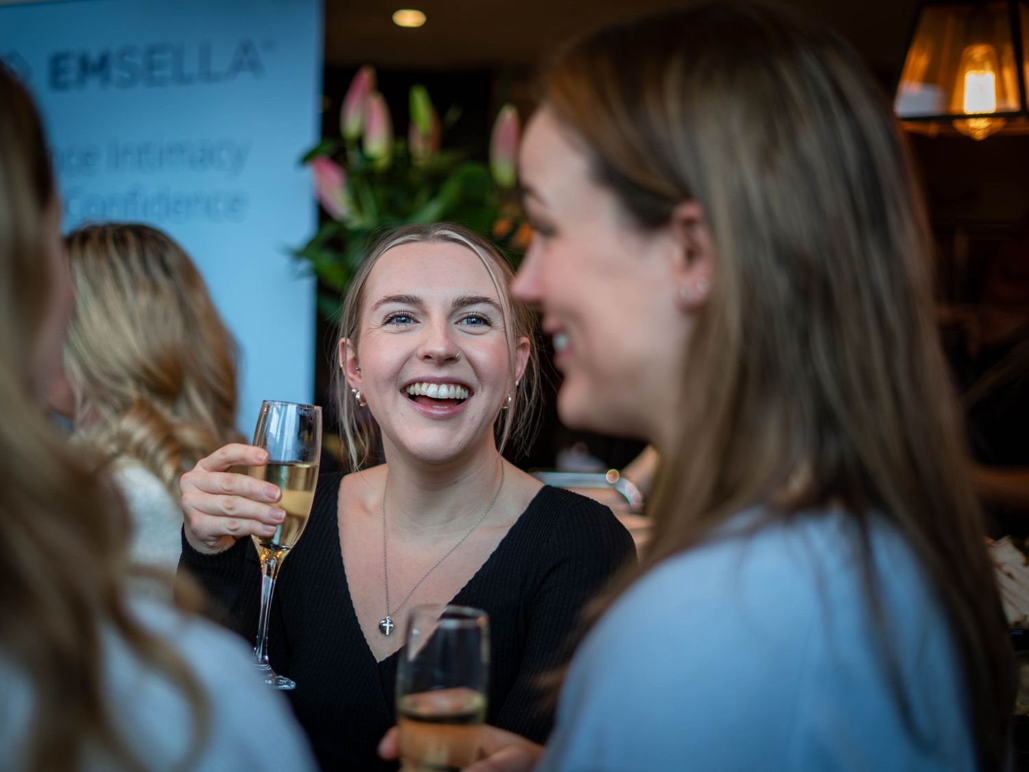 Two women smiling and holding champagne glasses at an Emsella intimacy conference networking event.