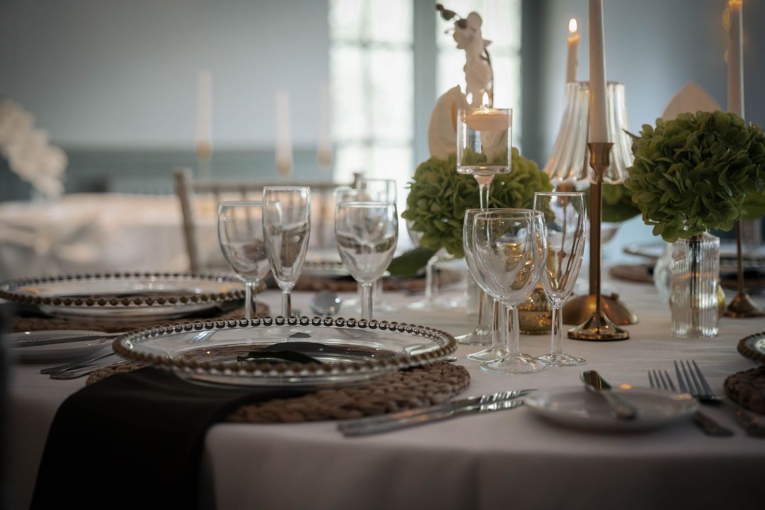Elegant wedding table setting with crystal glasses, decorative charger plates, and floral centerpieces on a white tablecloth.