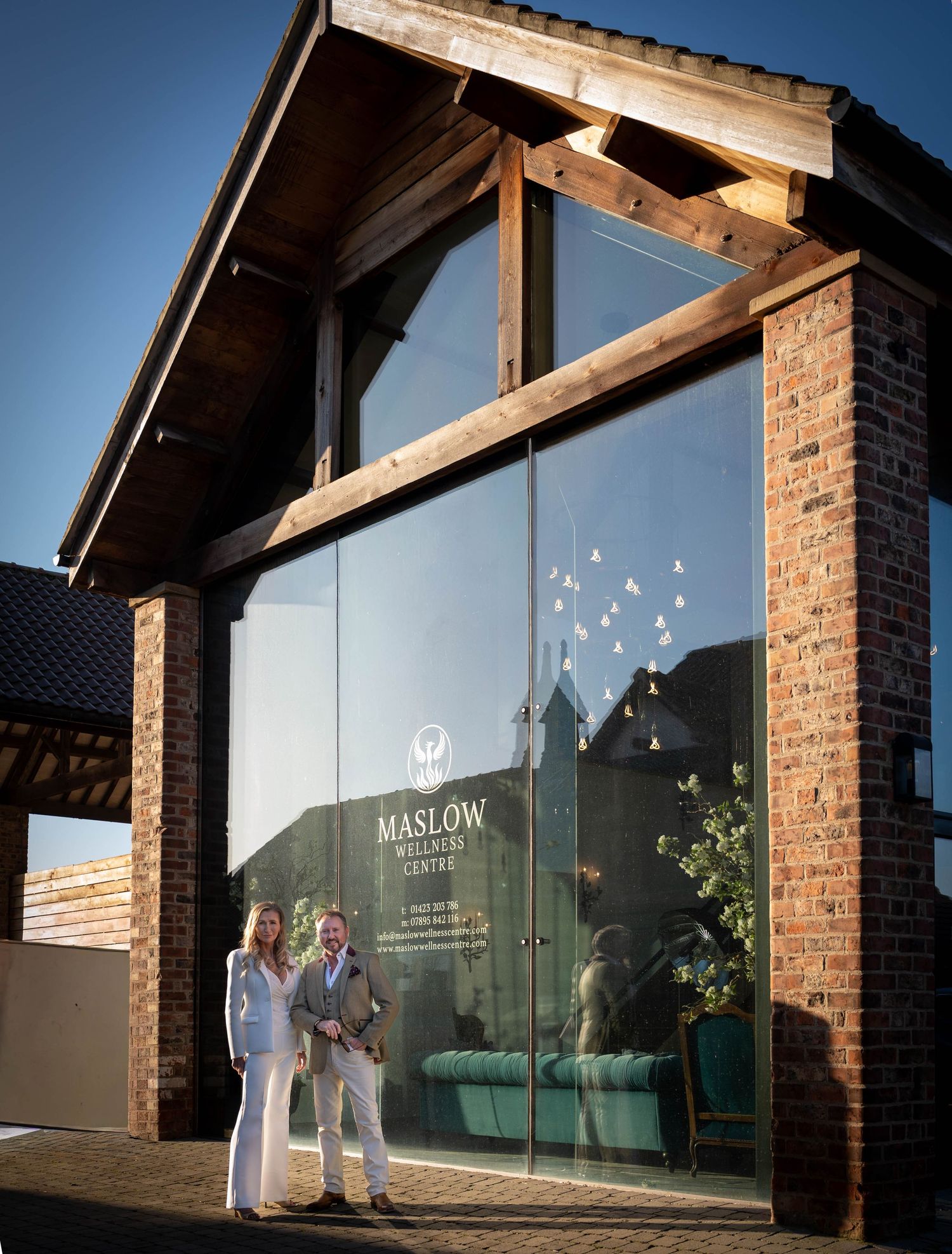 Modern brick building entrance with glass doors and wooden beams reflecting golden sunlight at dusk.