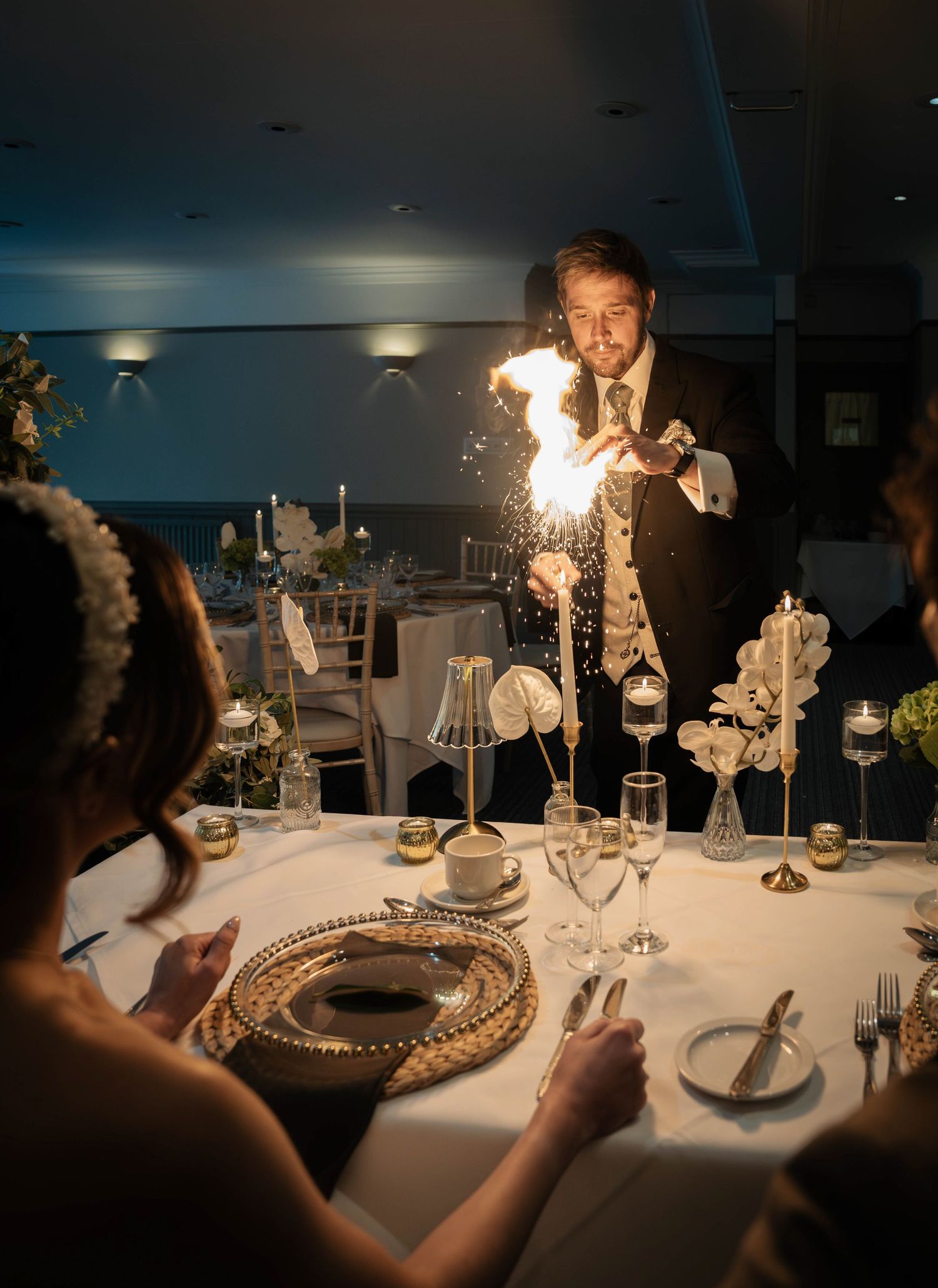 A groom performs a dazzling fire display at an elegant wedding reception dinner table with candles and floral decor.