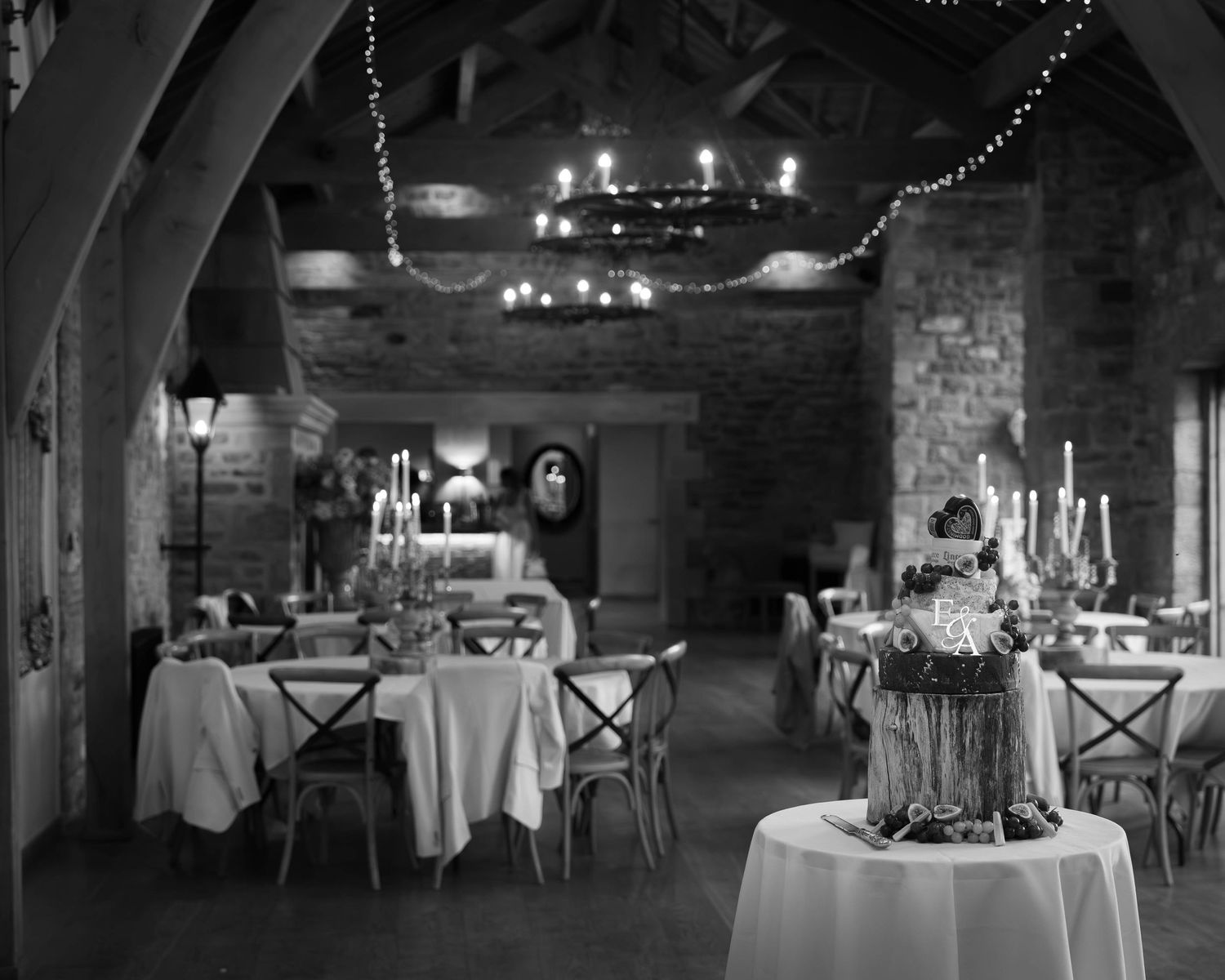 Elegant black and white photo of a candlelit rustic stone venue set for a formal dinner event.
