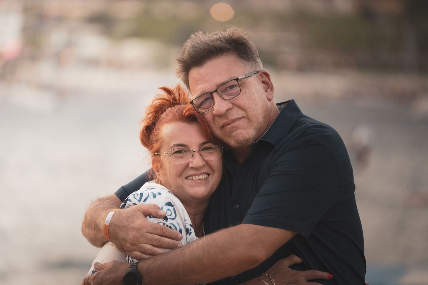 A couple shares a tender embrace against a soft sunset backdrop.
