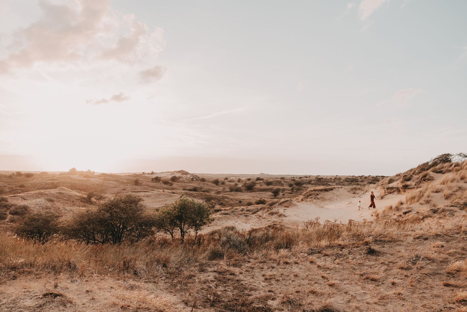 Mama en dochter wandelen in de duinen tijdens een fotoshoot met zonsondergang.