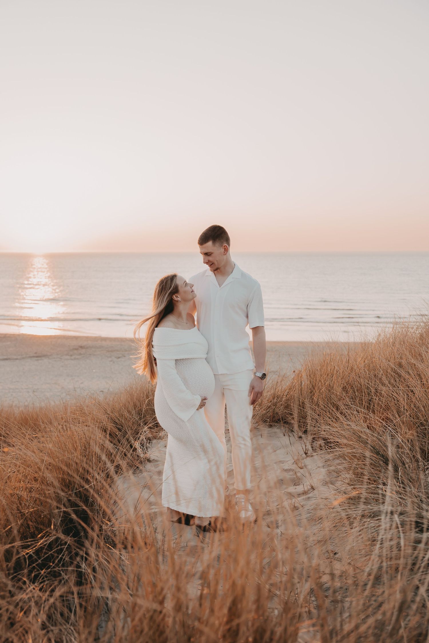 Koppel geeft elkaar een kus tijdens een fotoshoot op het strand bij zonsondergang.