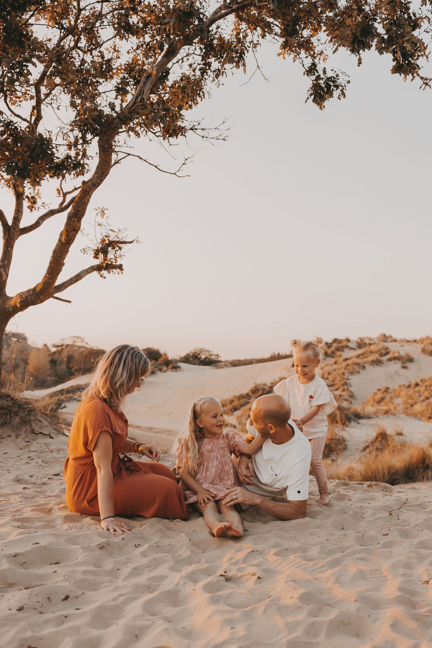 Een gezin klets met elkaar in het zand tijdens een gezinsfotoshoot met zonsondergang.
