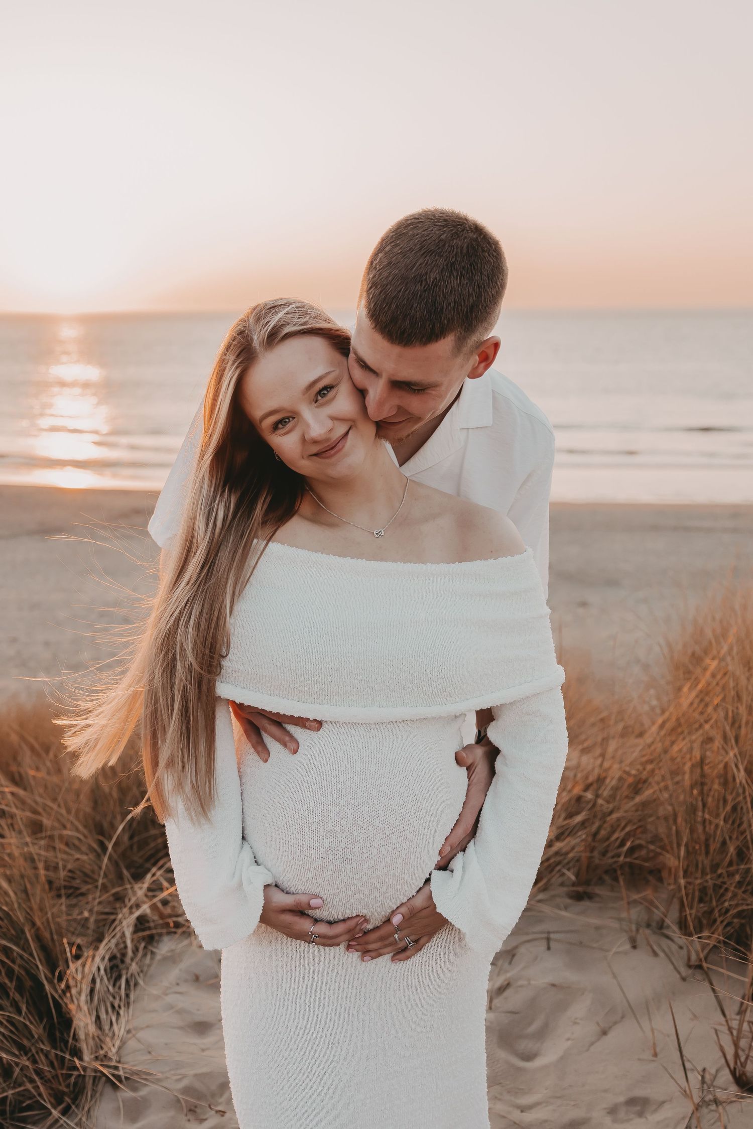 Koppel geeft elkaar een kus tijdens een fotoshoot op het strand bij zonsondergang.