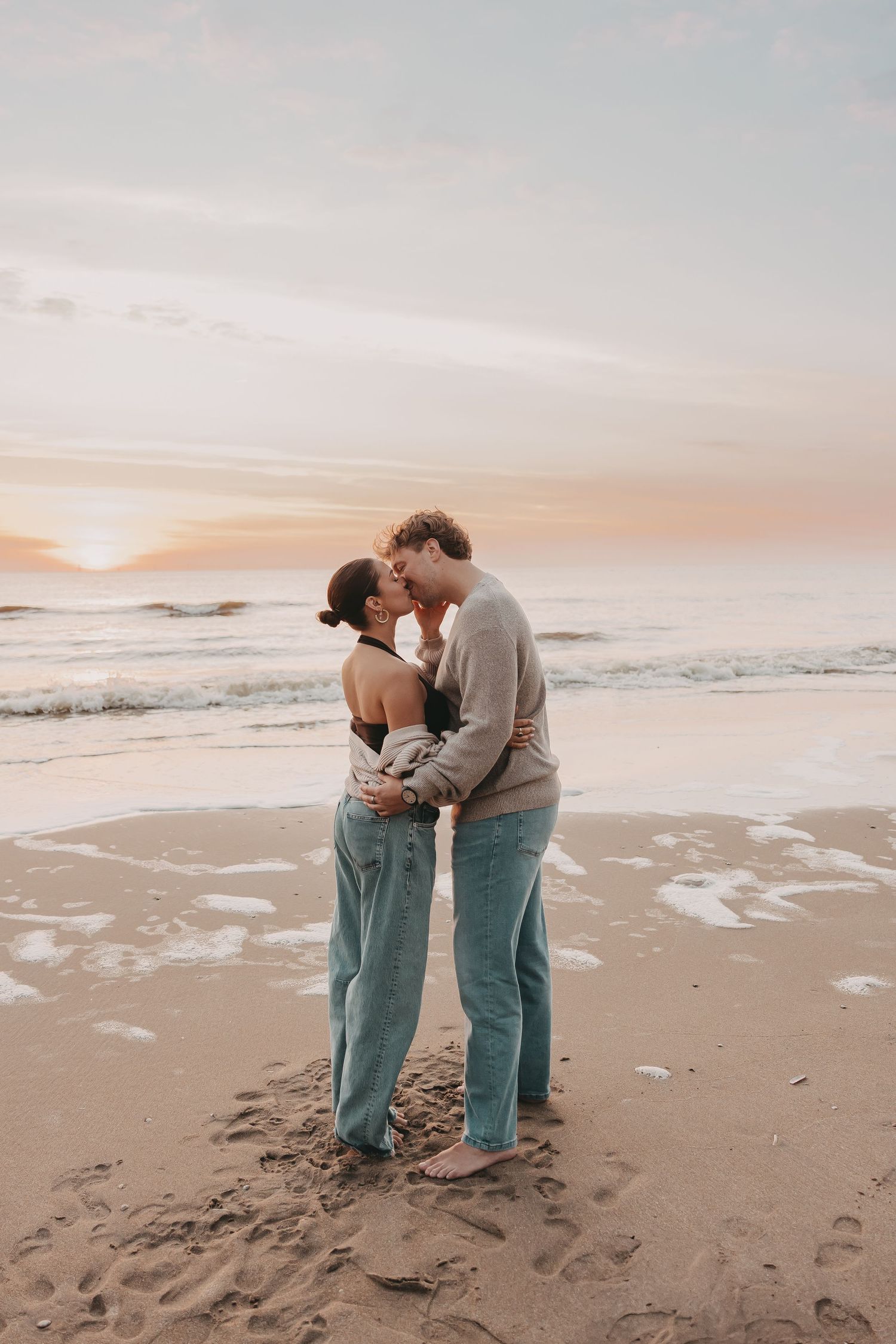 Koppel geeft elkaar een kus tijdens een fotoshoot op het strand bij zonsondergang.