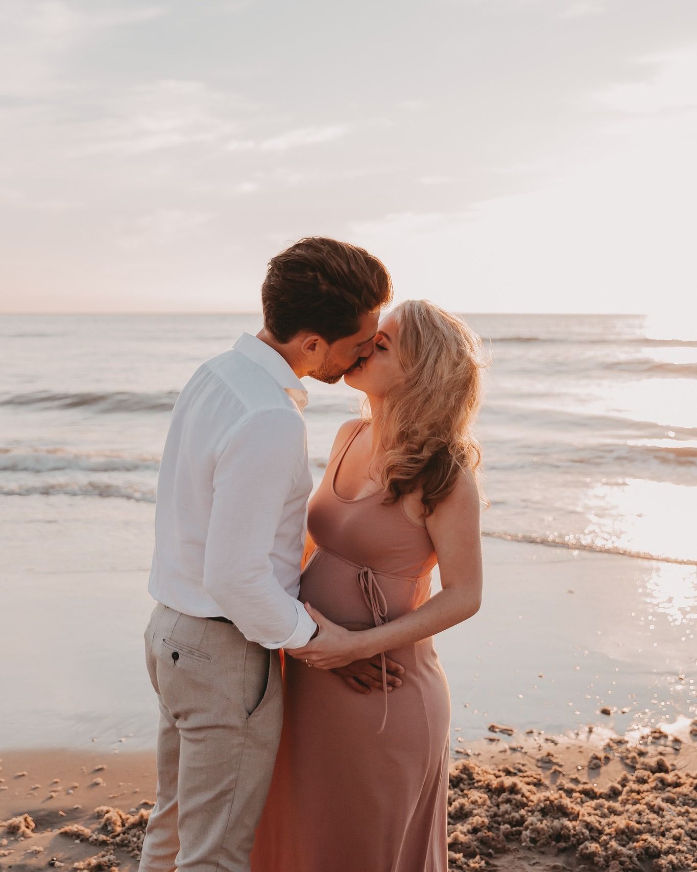 Koppel geeft elkaar een kus tijdens een fotoshoot op het strand bij zonsondergang.