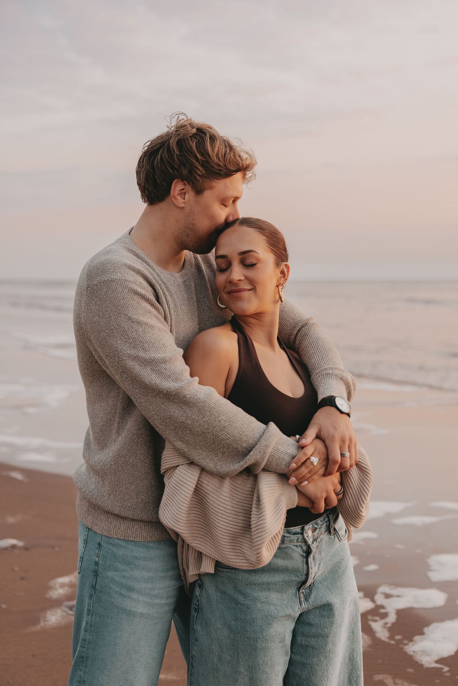 Koppel geeft elkaar een kus tijdens een fotoshoot op het strand bij zonsondergang.