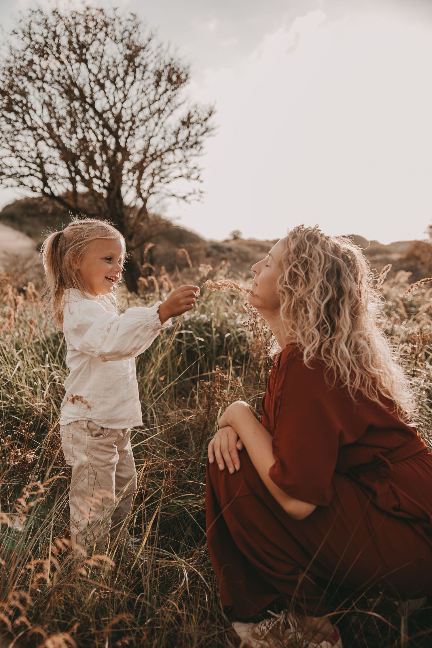 Dochter en mama plukken gras tijdens een fotoshoot in de duinen met zonsondergang.