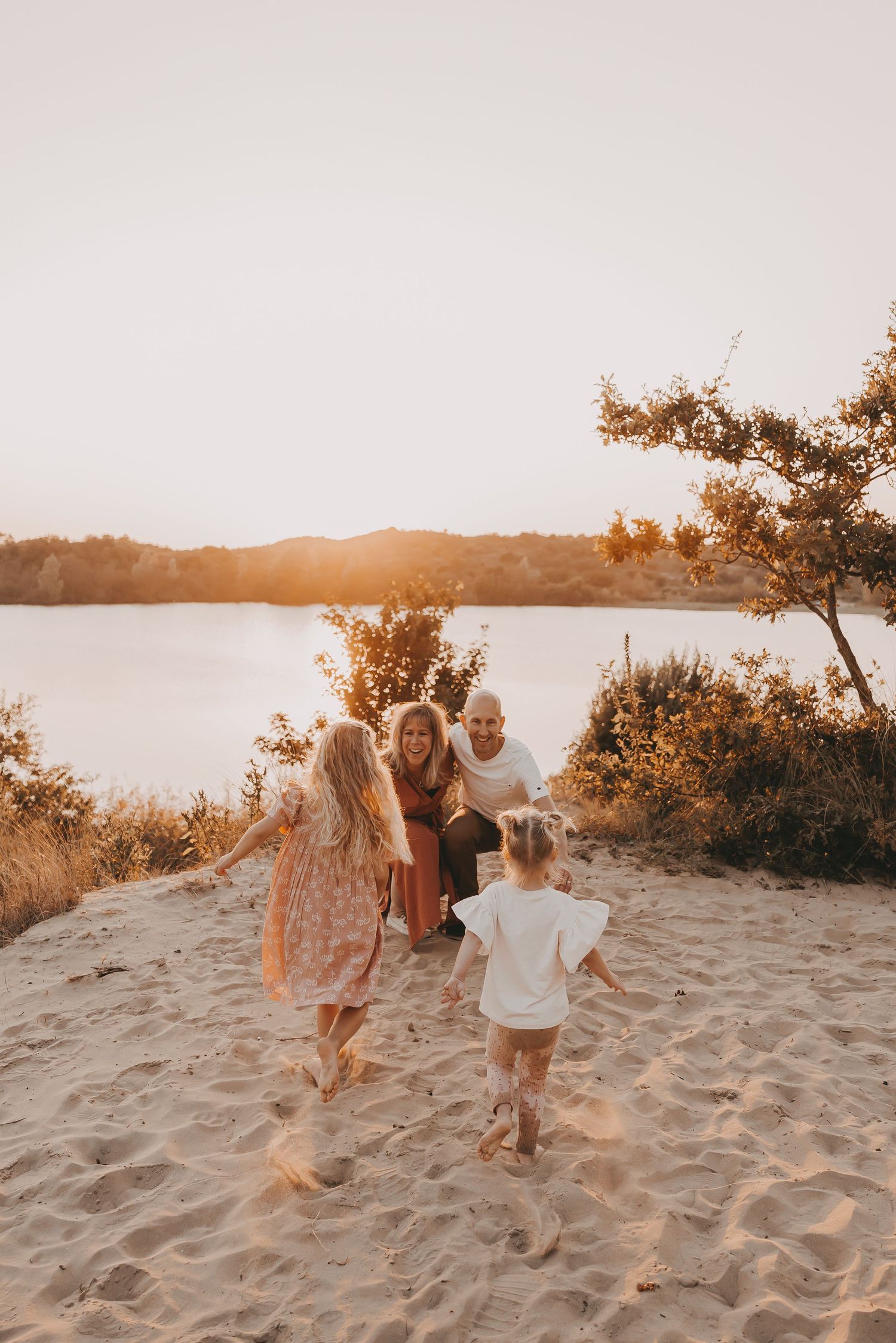 Twee kinderen rennen naar papa en mama tijdens een gezinsfotoshoot tijdens golden hour.