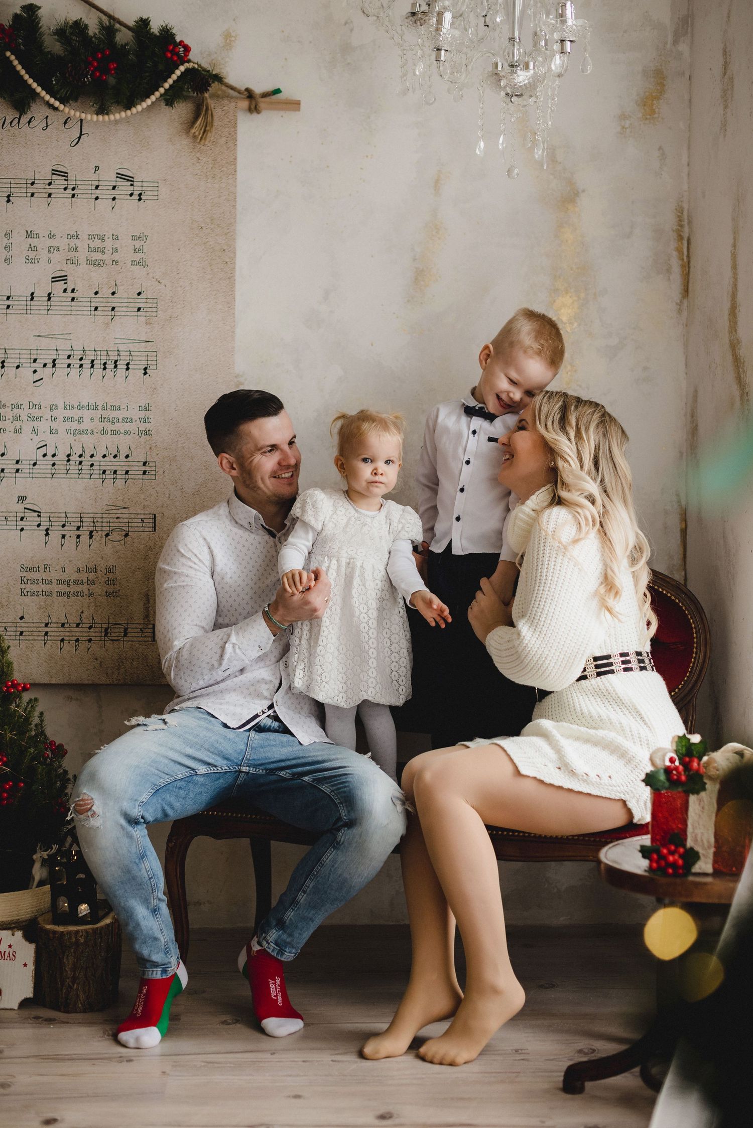 Family of four poses for a festive Christmas photo with holiday decorations in a cozy studio setting.