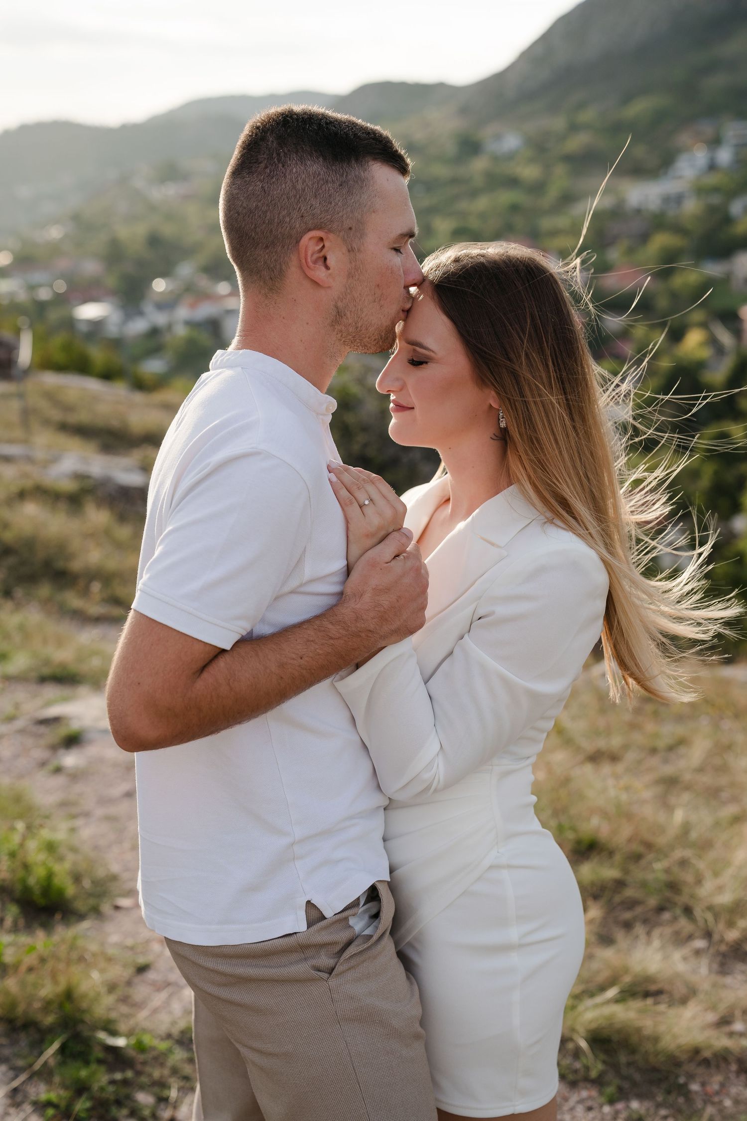 A tender moment between a couple in matching white outfits against a mountain backdrop.