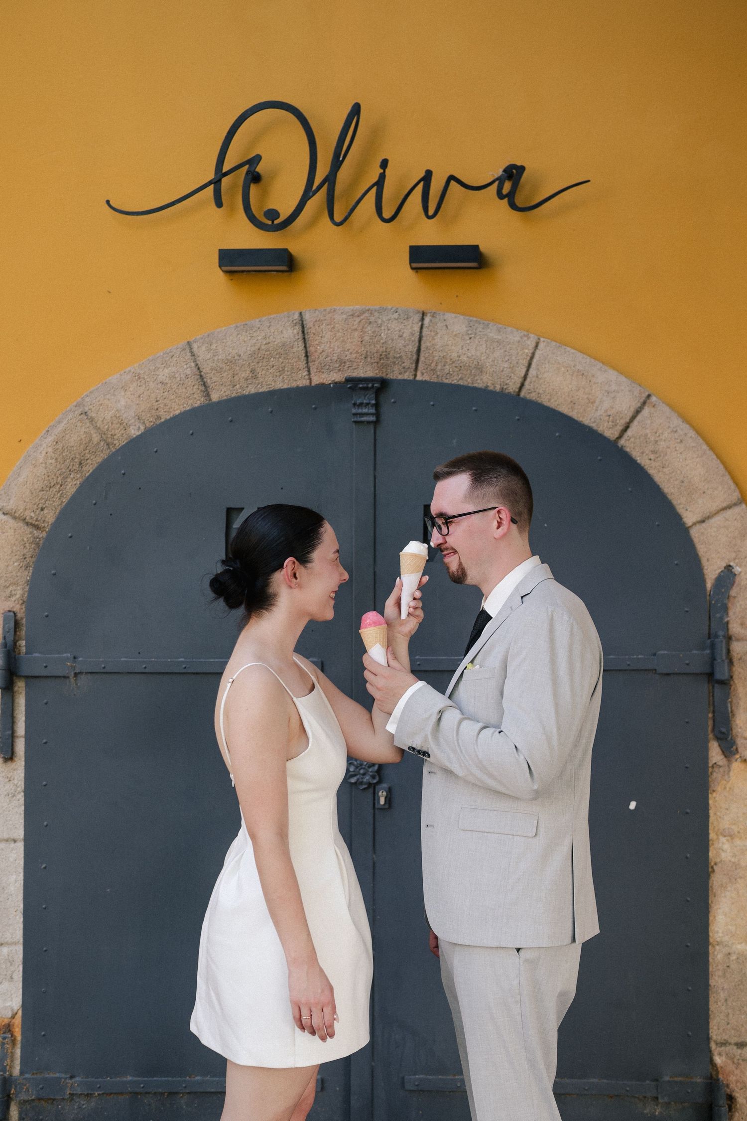 Couple shares a playful moment against yellow wall with arched doorways.