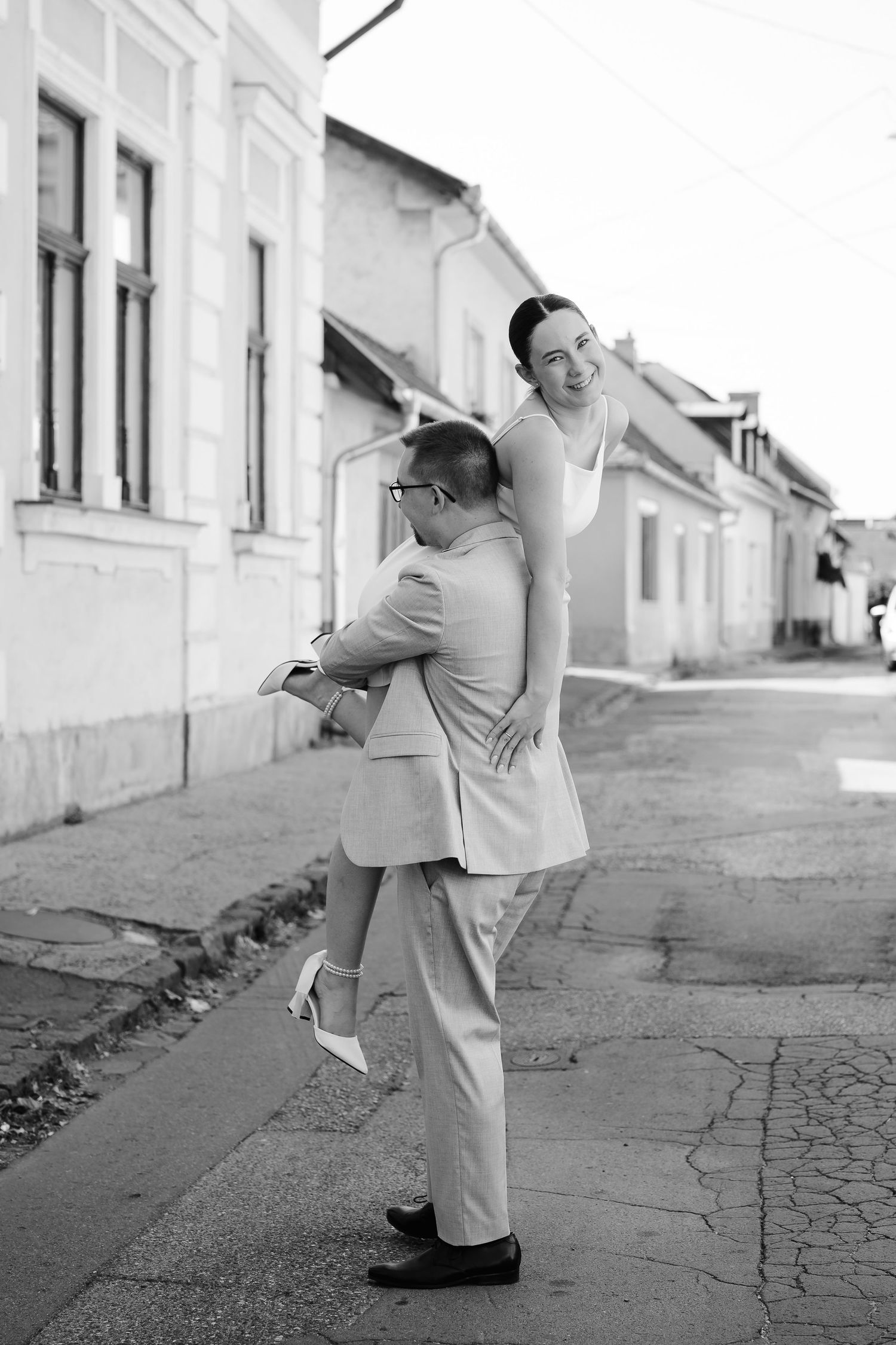 Black and white photo of a couple dancing playfully on a cobblestone street.