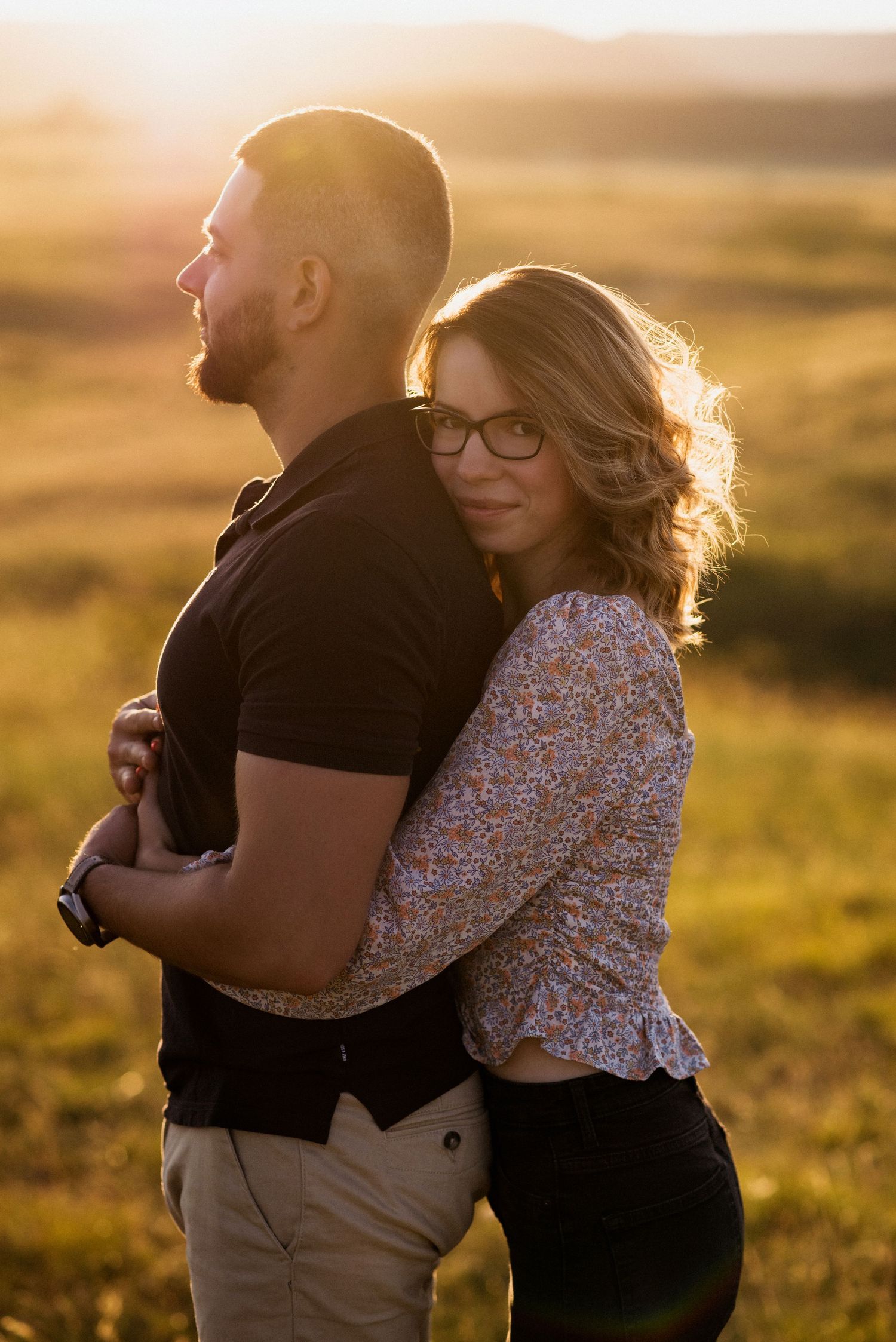 Couple embracing in golden sunset light with mountains in the background.