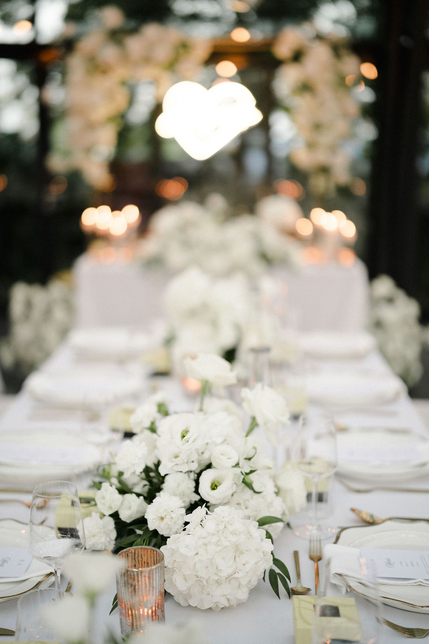 Elegant white floral wedding reception table setting with candlelight and place settings.