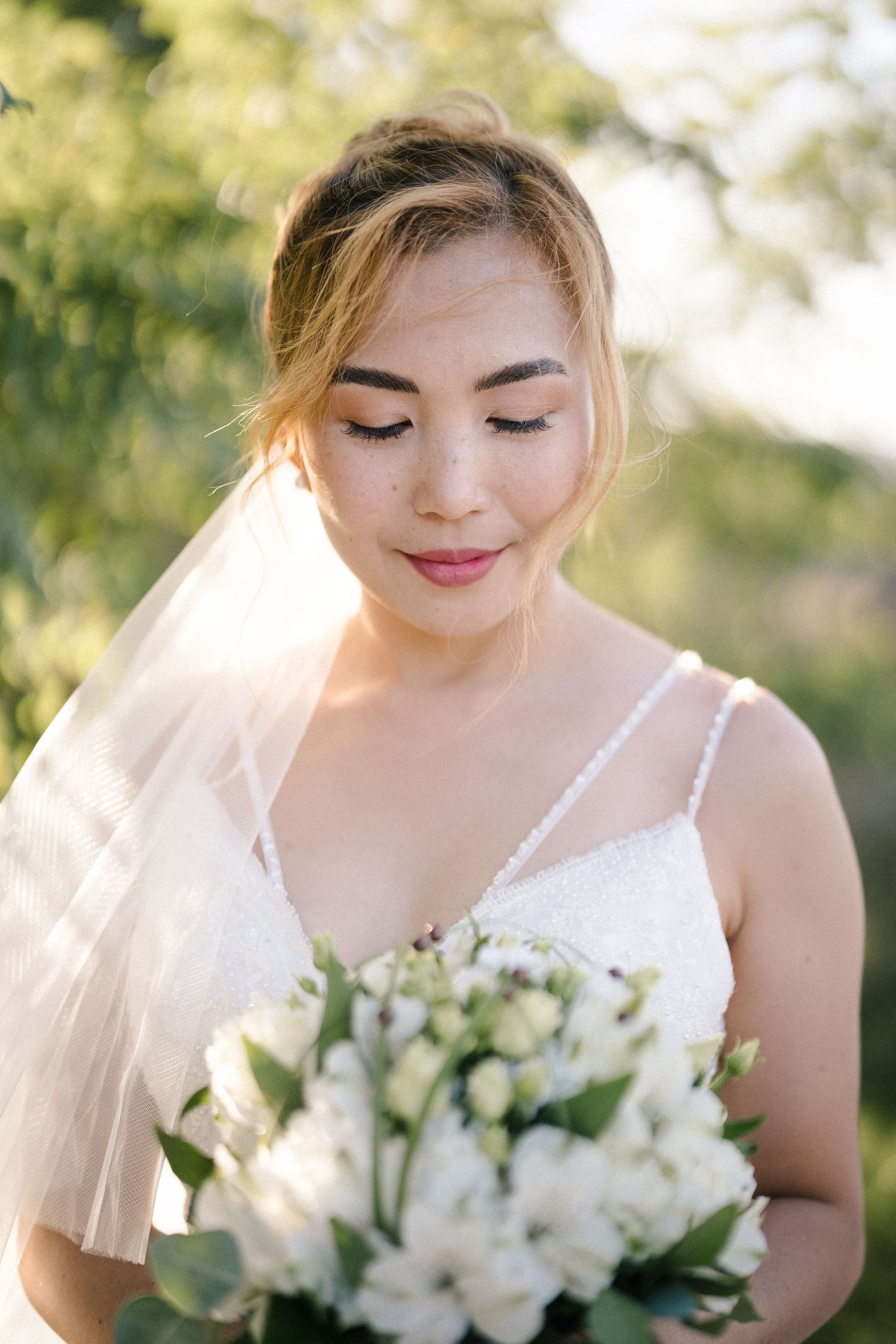 Delicate white bridal bouquet with roses and greenery in soft natural lighting.