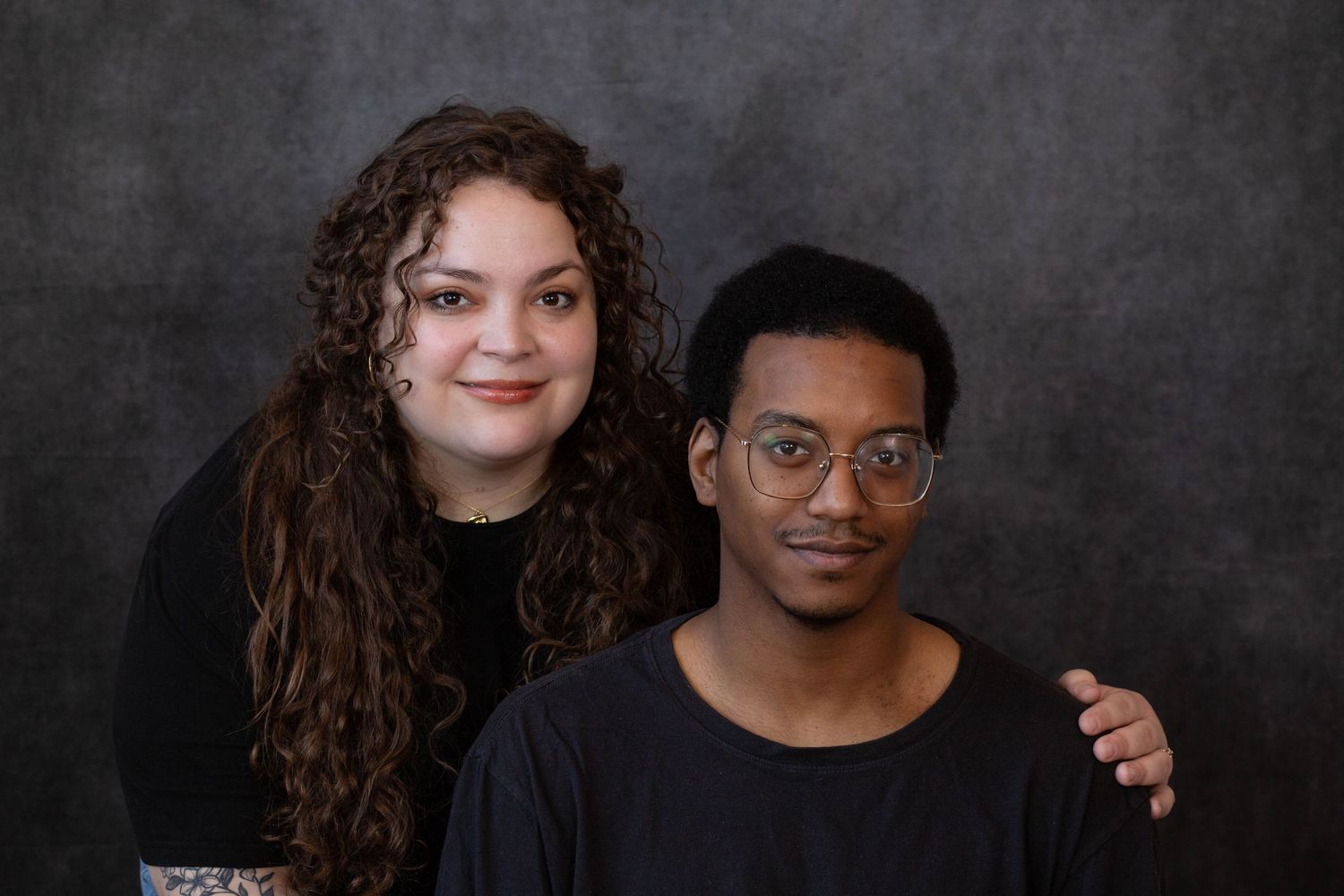 Two people smiling and embracing while posing for a professional photo against a dark background.