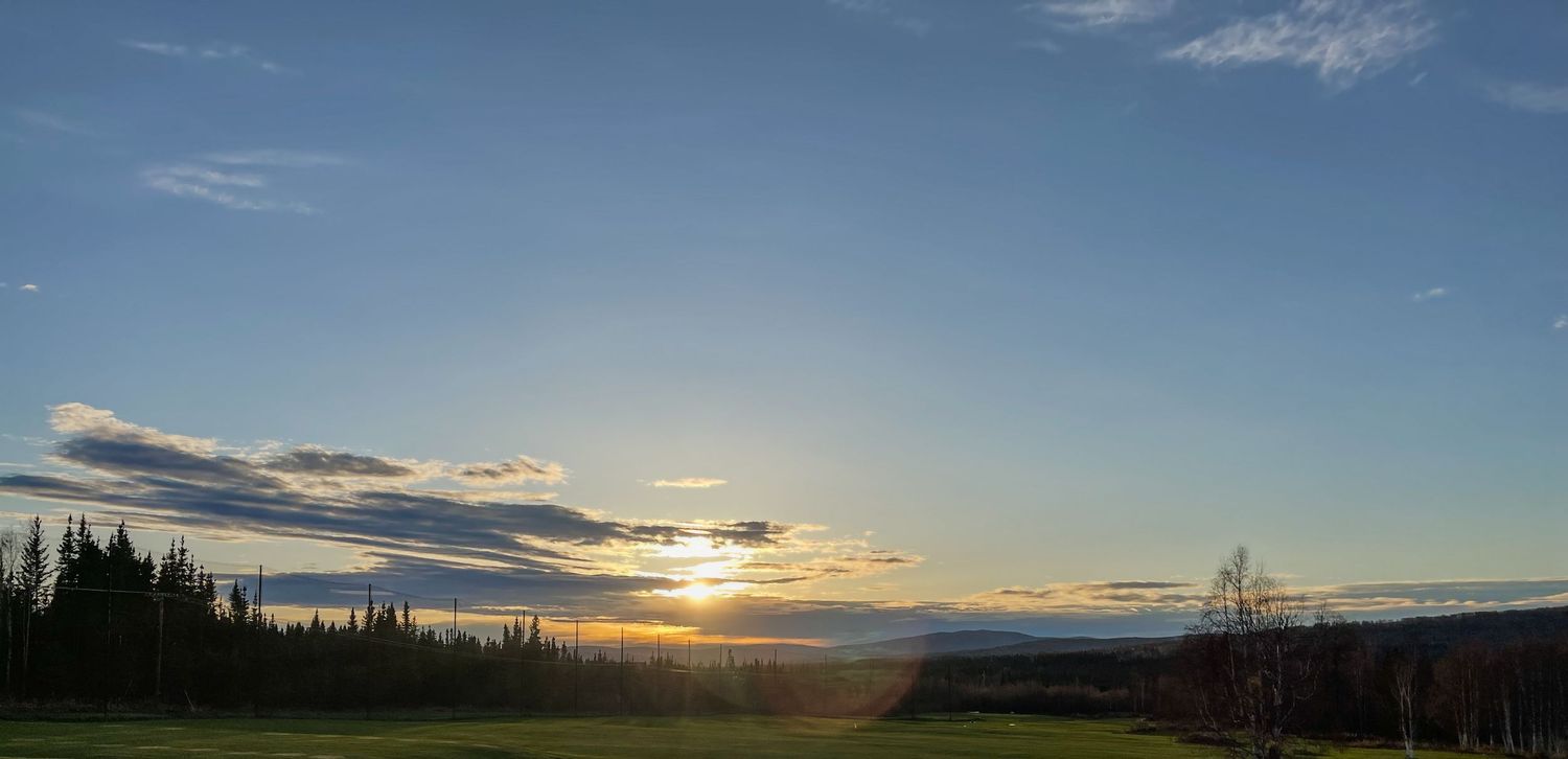 Panoramic landscape of snow-capped mountains and rolling hills under a dramatic cloudy sky at sunset.