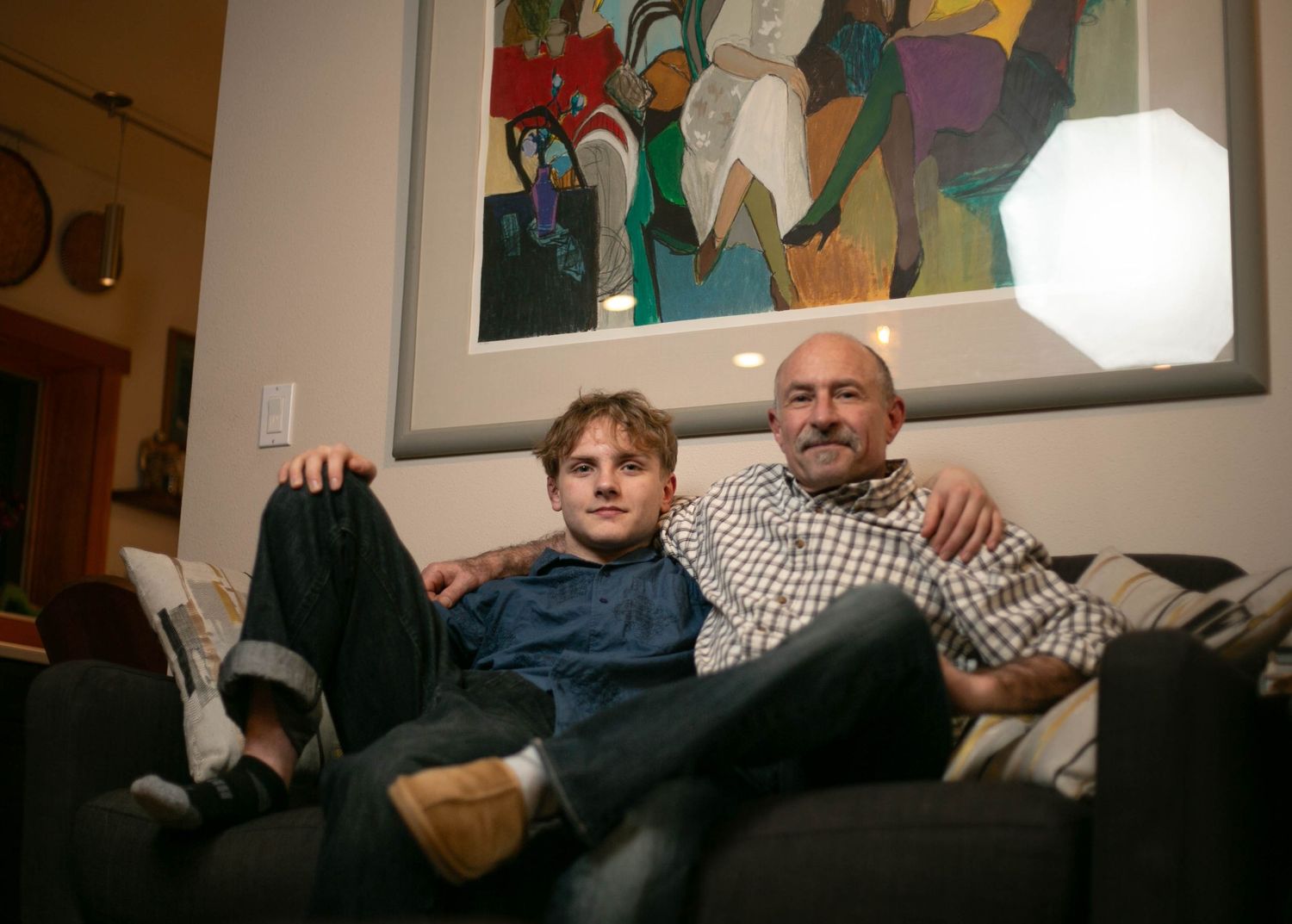 A group relaxes together on a couch in a dimly lit living room setting.