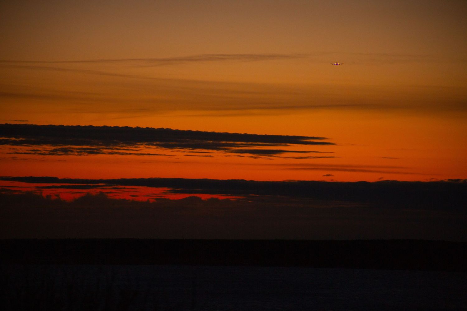 Stunning orange and red sunset over a dark horizon with silhouetted clouds and birds flying in the twilight sky.