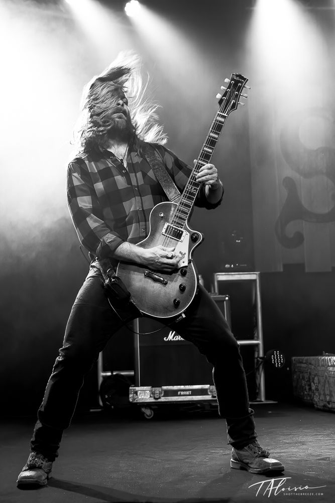 Black and white concert photo of guitarist performing energetically on stage.