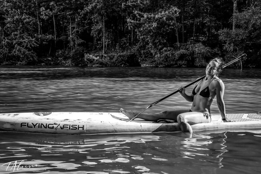 Black and white image of people paddleboarding on calm water.