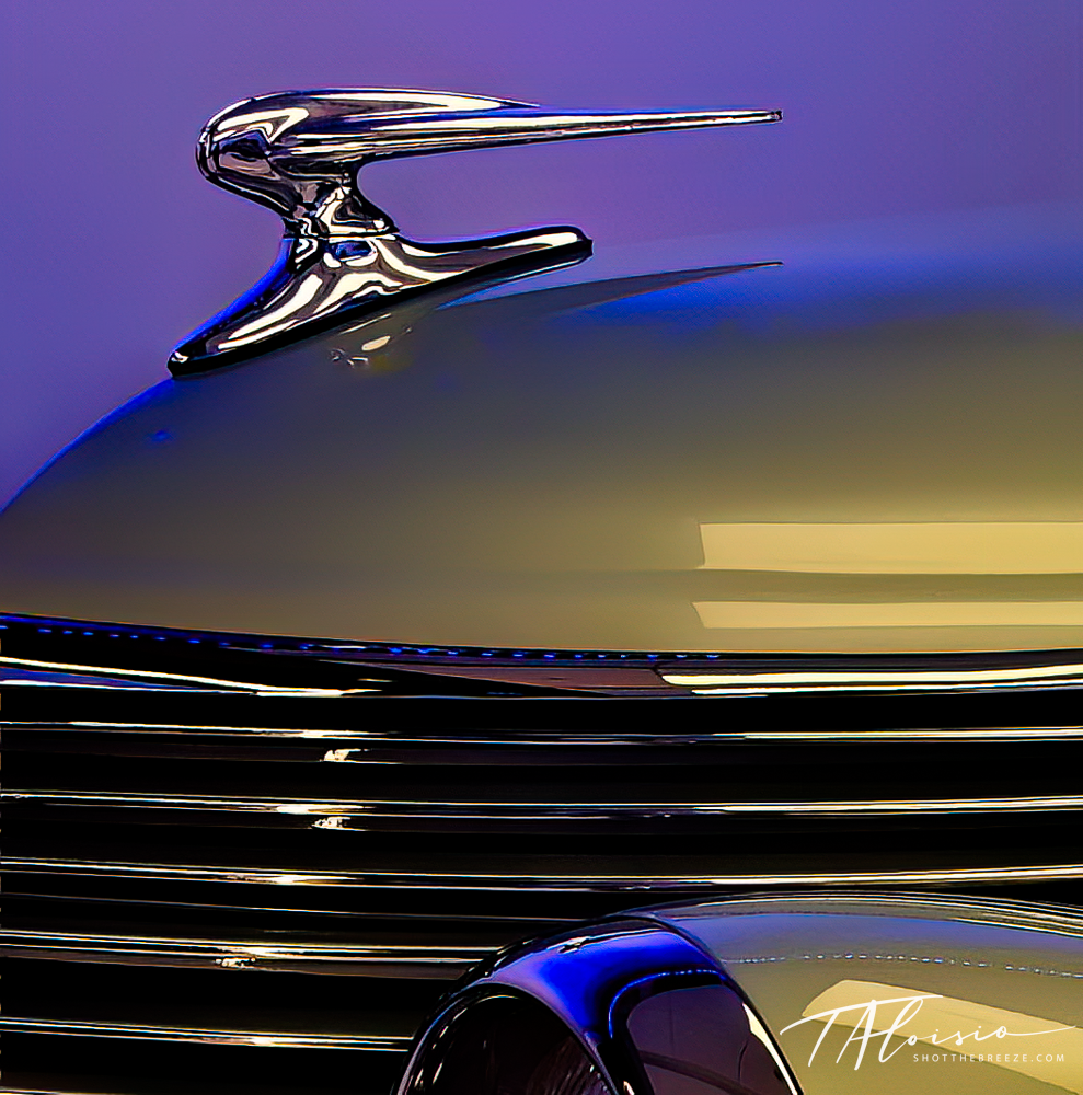 Abstract chrome car hood ornament silhouette against a purple and gold gradient sky.