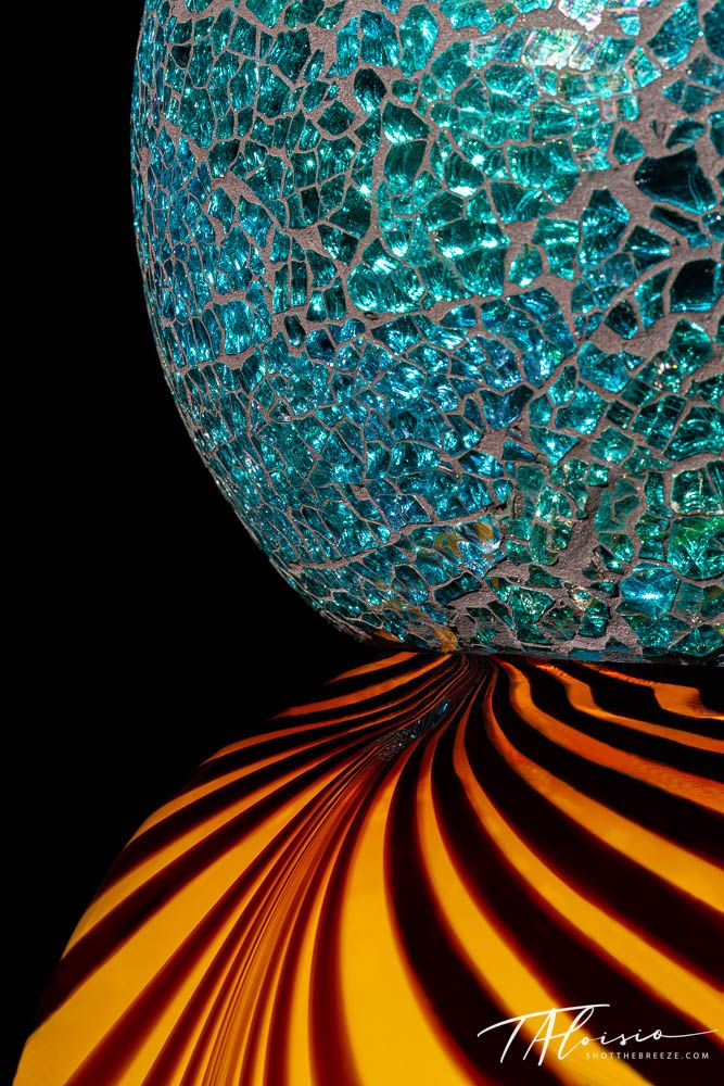 Turquoise crackled glass sphere sitting on orange striped surface in dramatic lighting.