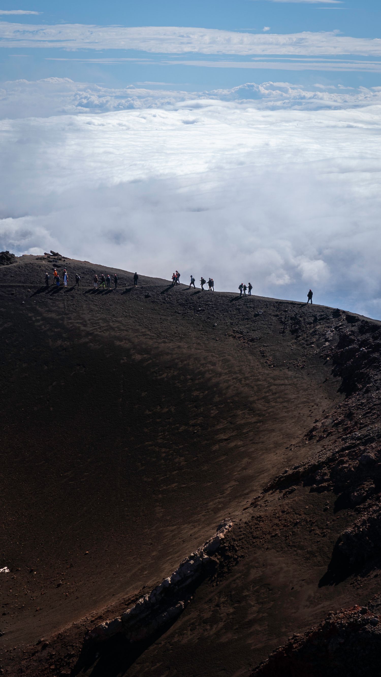 Escursionisti sul cratere dell’Etna sopra le nuvole, paesaggio vulcanico siciliano.
