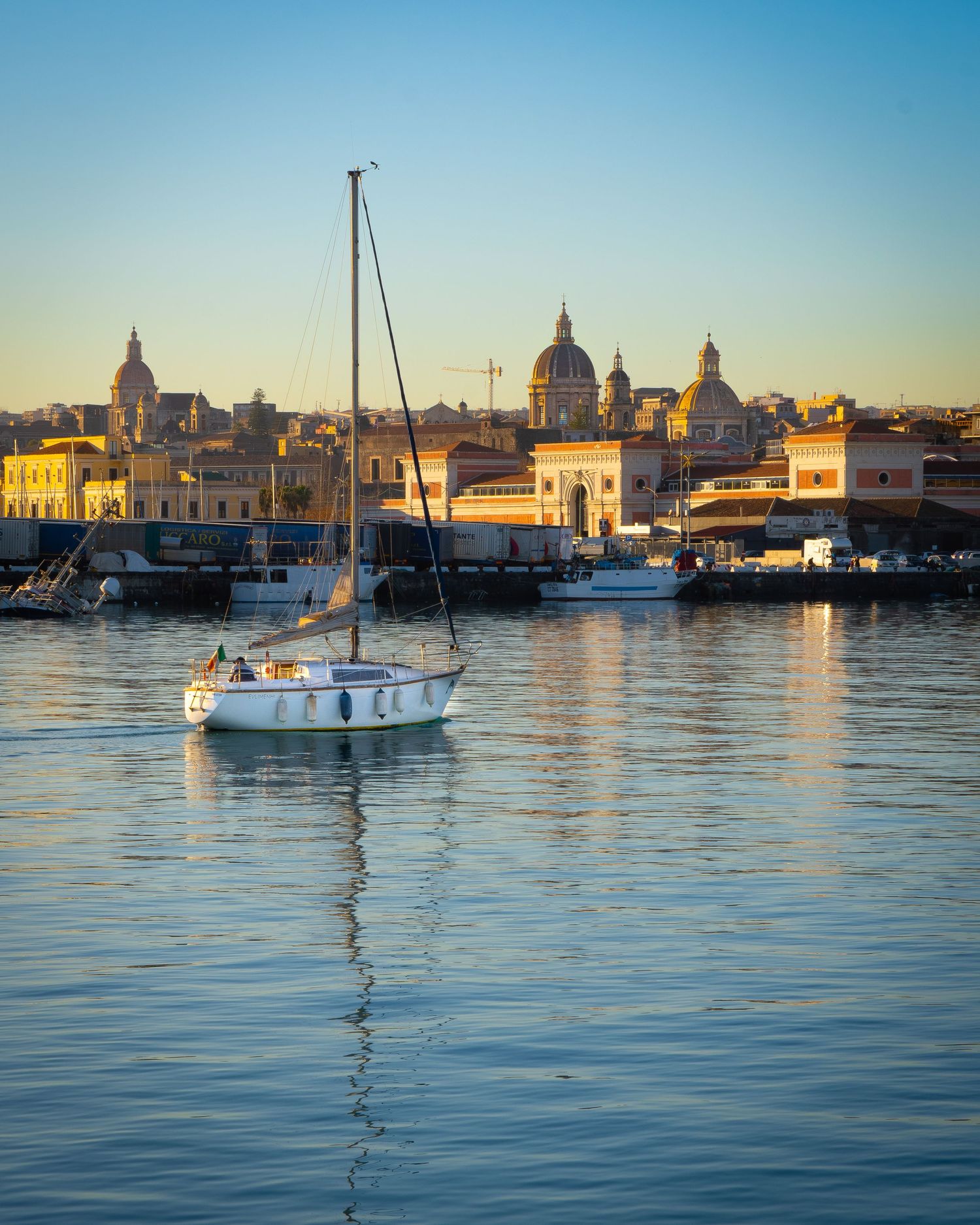 Barca a vela nel porto di Catania al tramonto, fotografia marittima mediterranea.