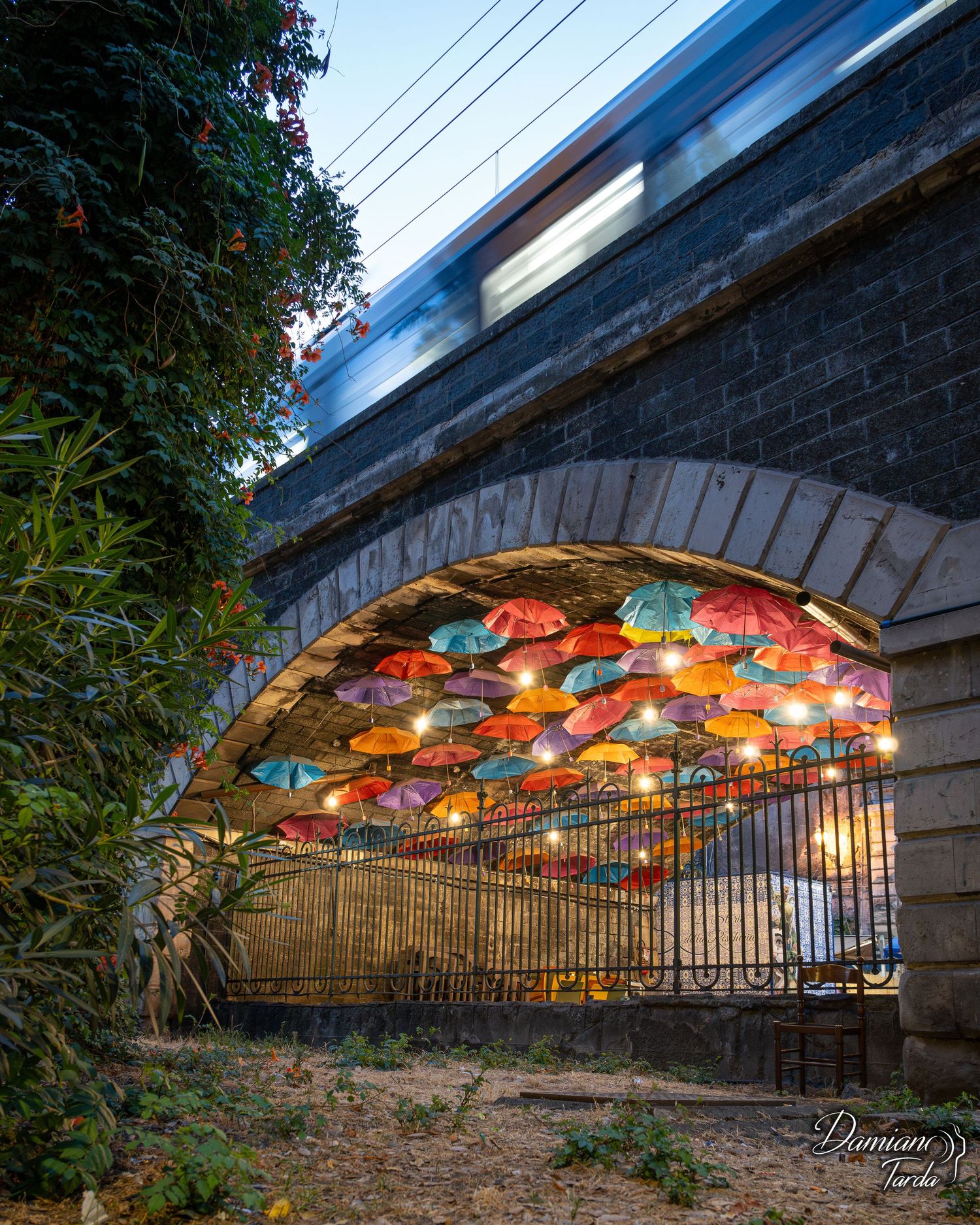 Ombrelli colorati sotto gli archi della marina, passaggio del treno, fotografia urbana creativa.