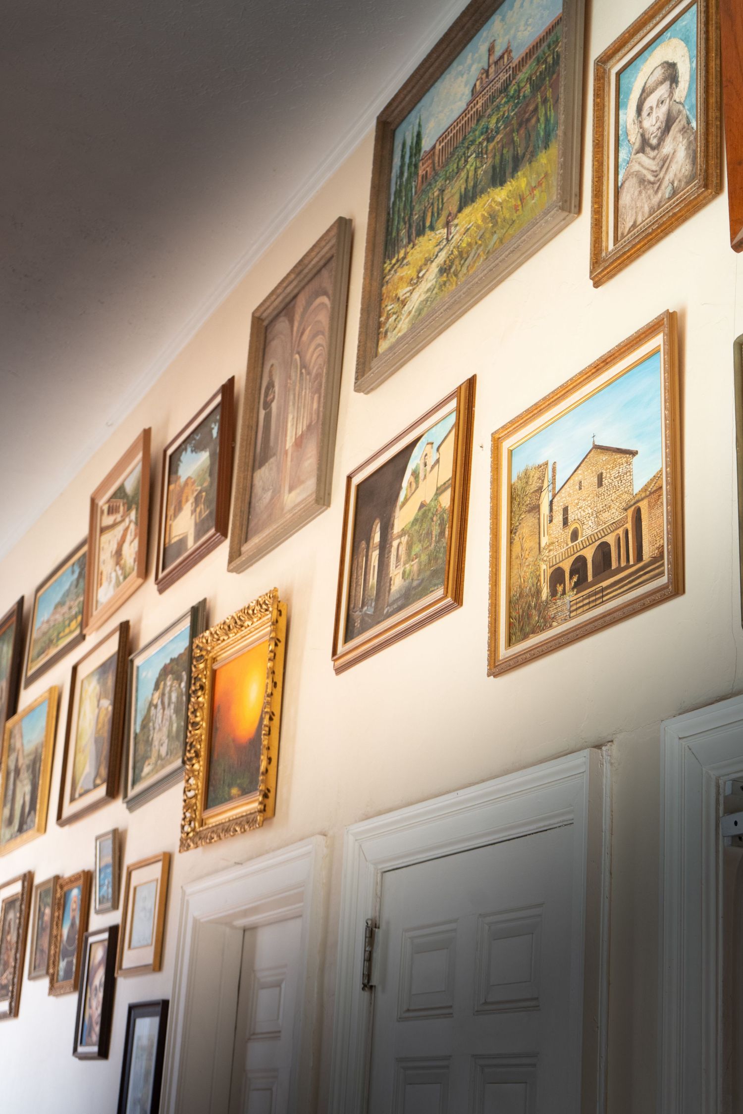 A gallery wall displays multiple framed paintings and artwork arranged in a row along a white wall.