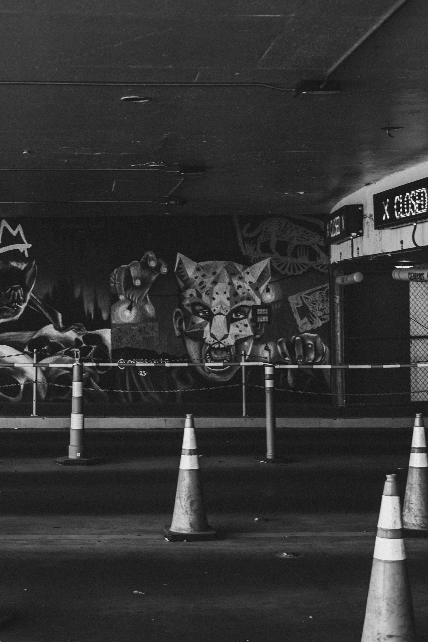 Black and white photo of a dimly lit parking garage interior with traffic cones and graffiti art on the walls.
