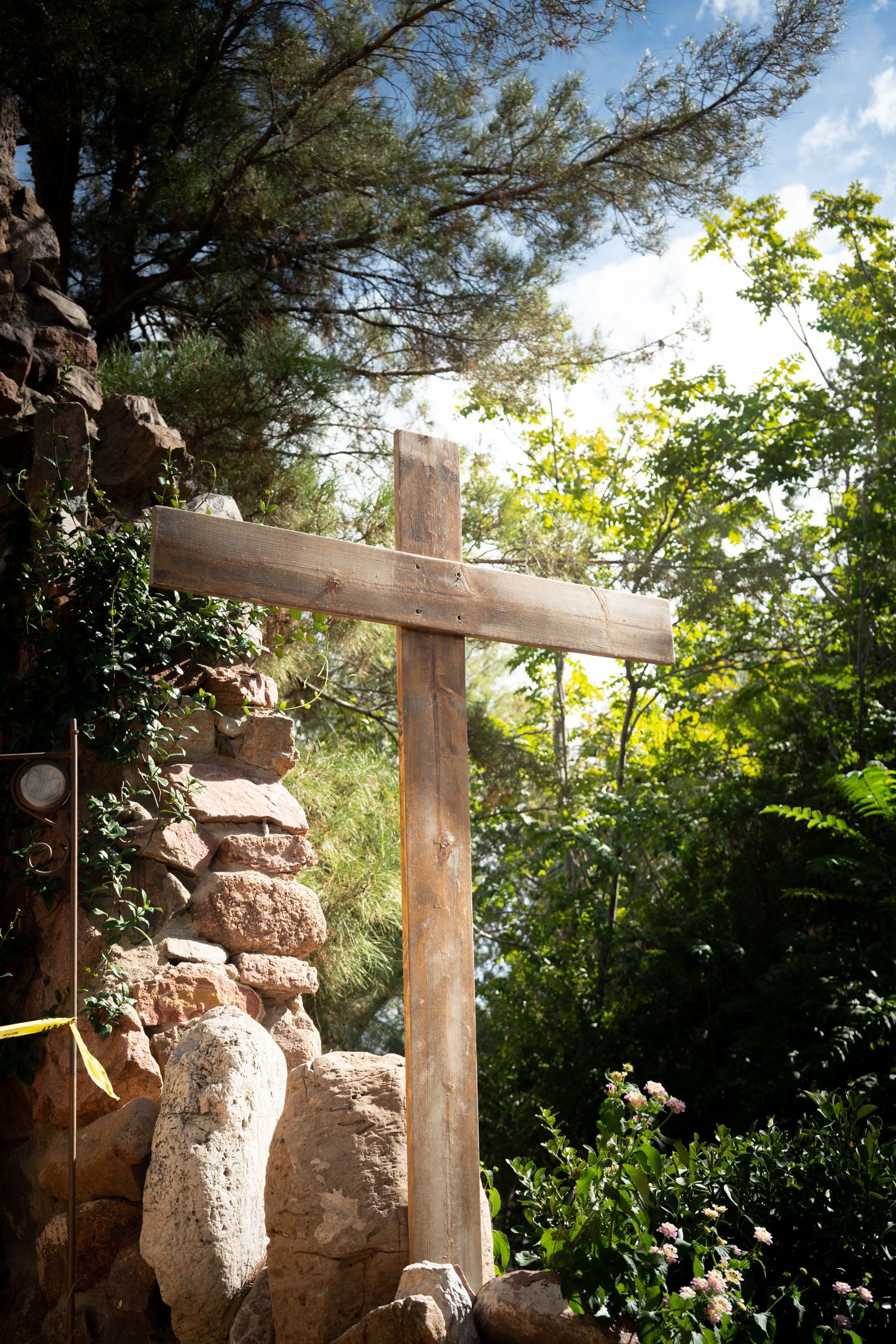 Rustic wooden gate posts and stone walls frame a sunlit garden path through lush greenery.
